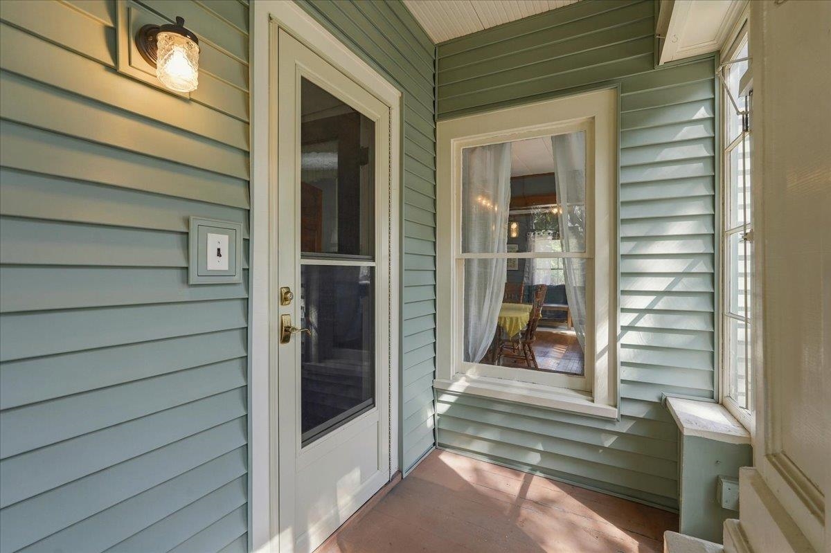 Covered front porch with green siding, white storm door, and windows overlooking a dining room.