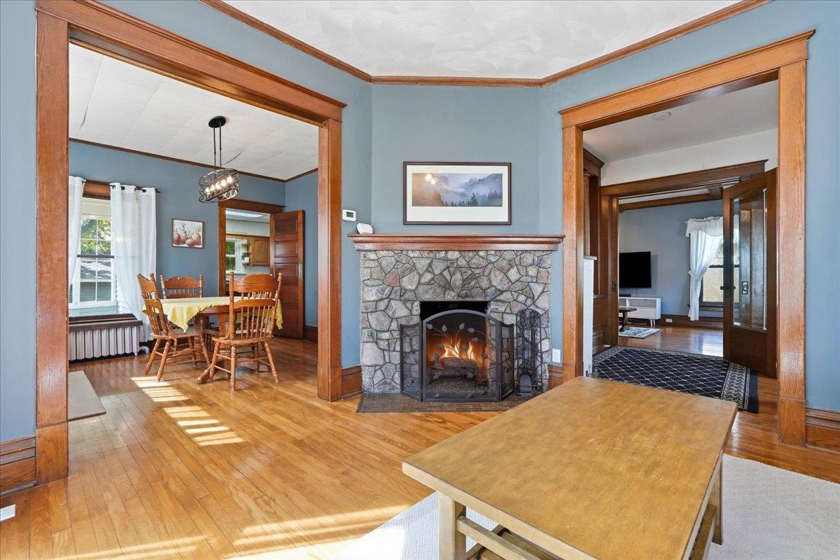 Living room with a stone fireplace, hardwood floors, and wide wood-trimmed openings to adjoining rooms.