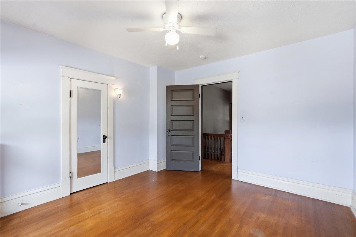 Empty room with polished hardwood floors, pale walls, and an open dark door to a landing.