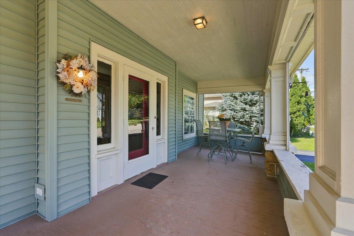 Covered front porch with a red entry door, flower wreath, and patio table and chairs.