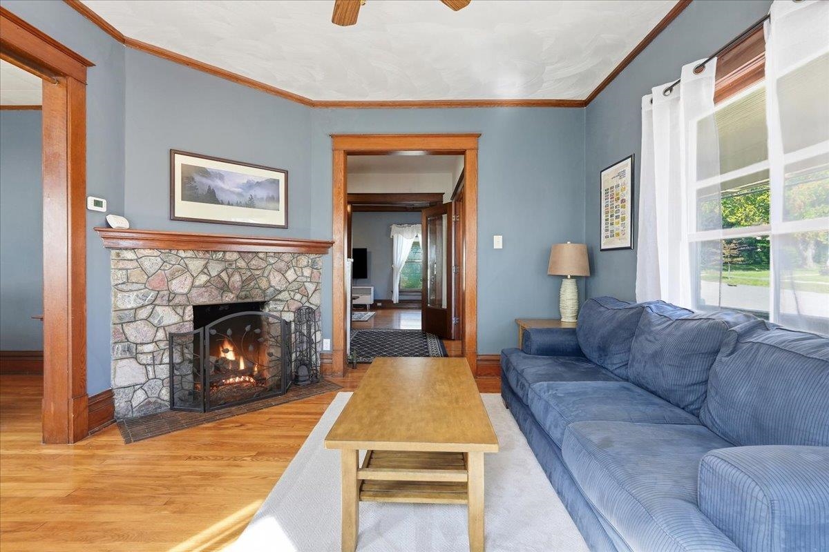 Living room with a stone fireplace, blue sectional sofa, hardwood floors, and large windows.