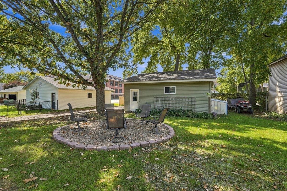 Backyard with a stone-edged gravel seating area, patio chairs, mature trees, and a detached green outbuilding.