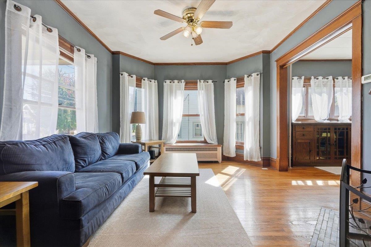 Living room with a blue sofa, hardwood floors, tall curtained windows, and warm wood trim.