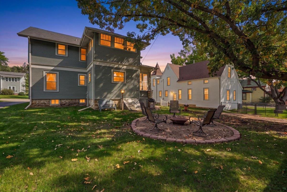 Two-story gray home with glowing windows and a circular fire-pit seating area in the backyard.
