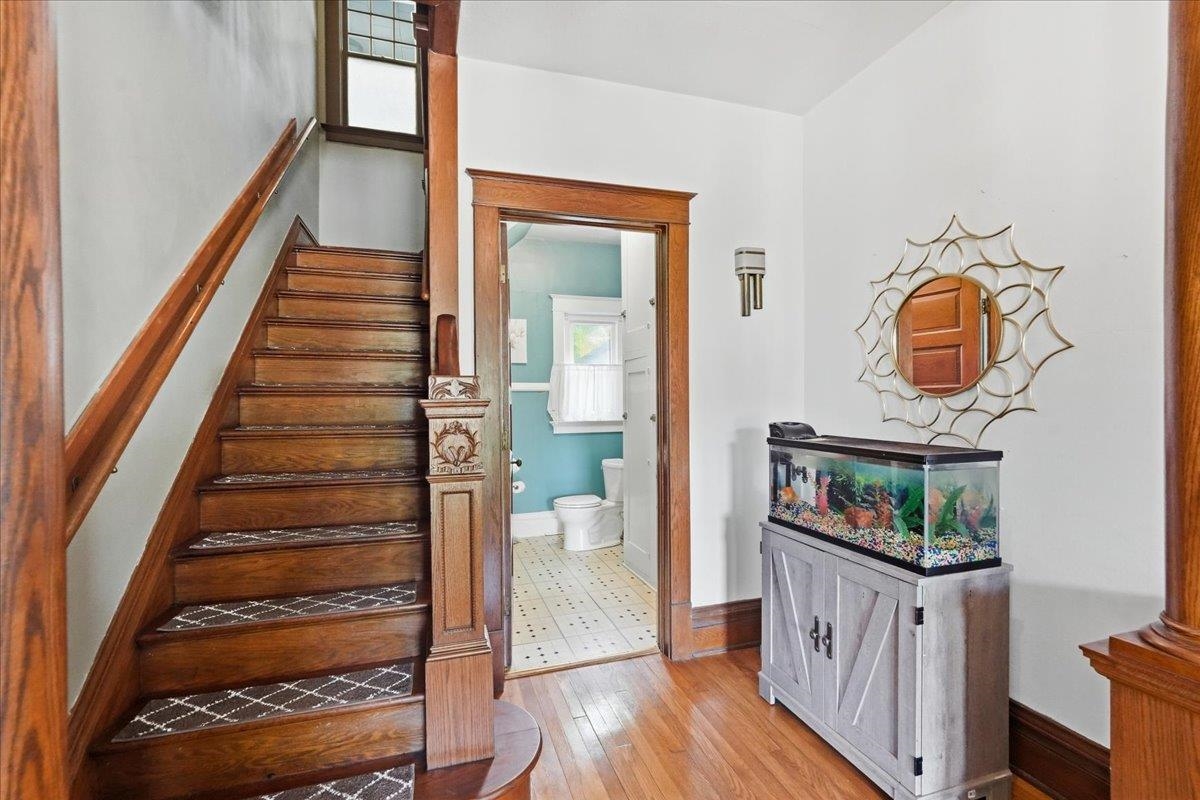 Entry foyer with a dark wood staircase, hardwood floors, and an aquarium beside the bathroom doorway.