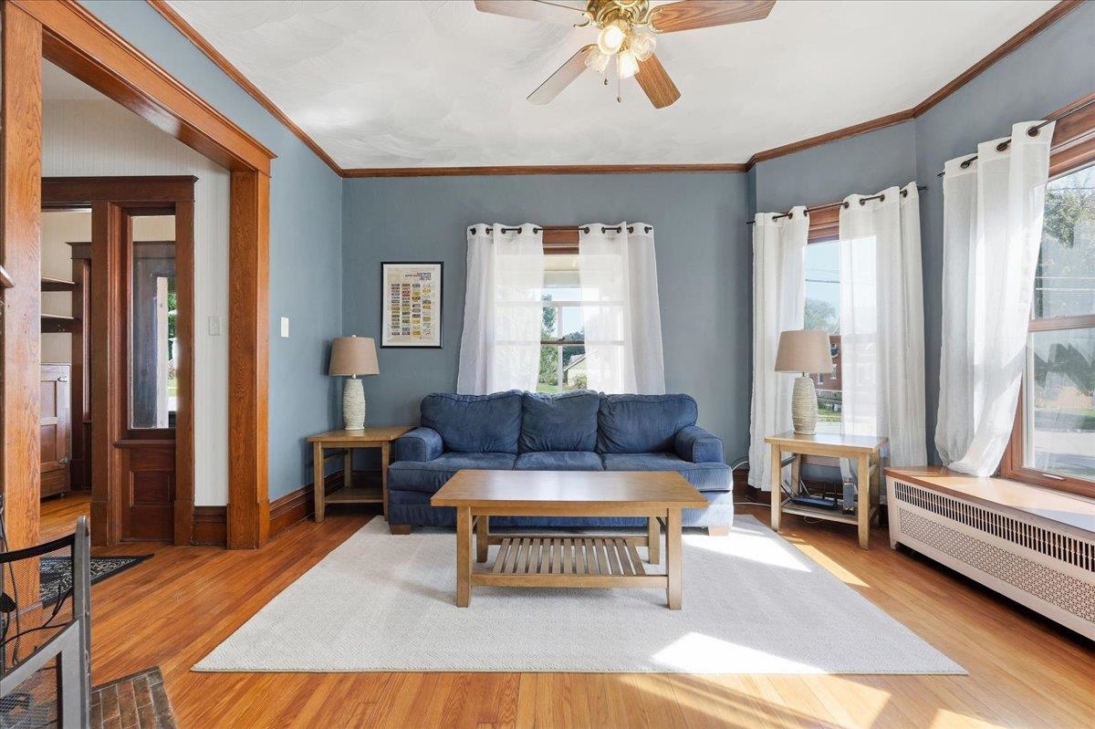 Living room with blue walls, dark wood trim, hardwood floors, and a blue sofa beneath large curtained windows.