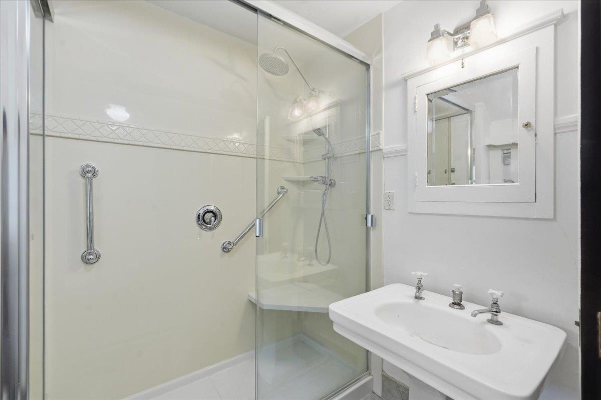 Bathroom with a glass shower, chrome grab bars, and a white sink beneath a framed mirror.