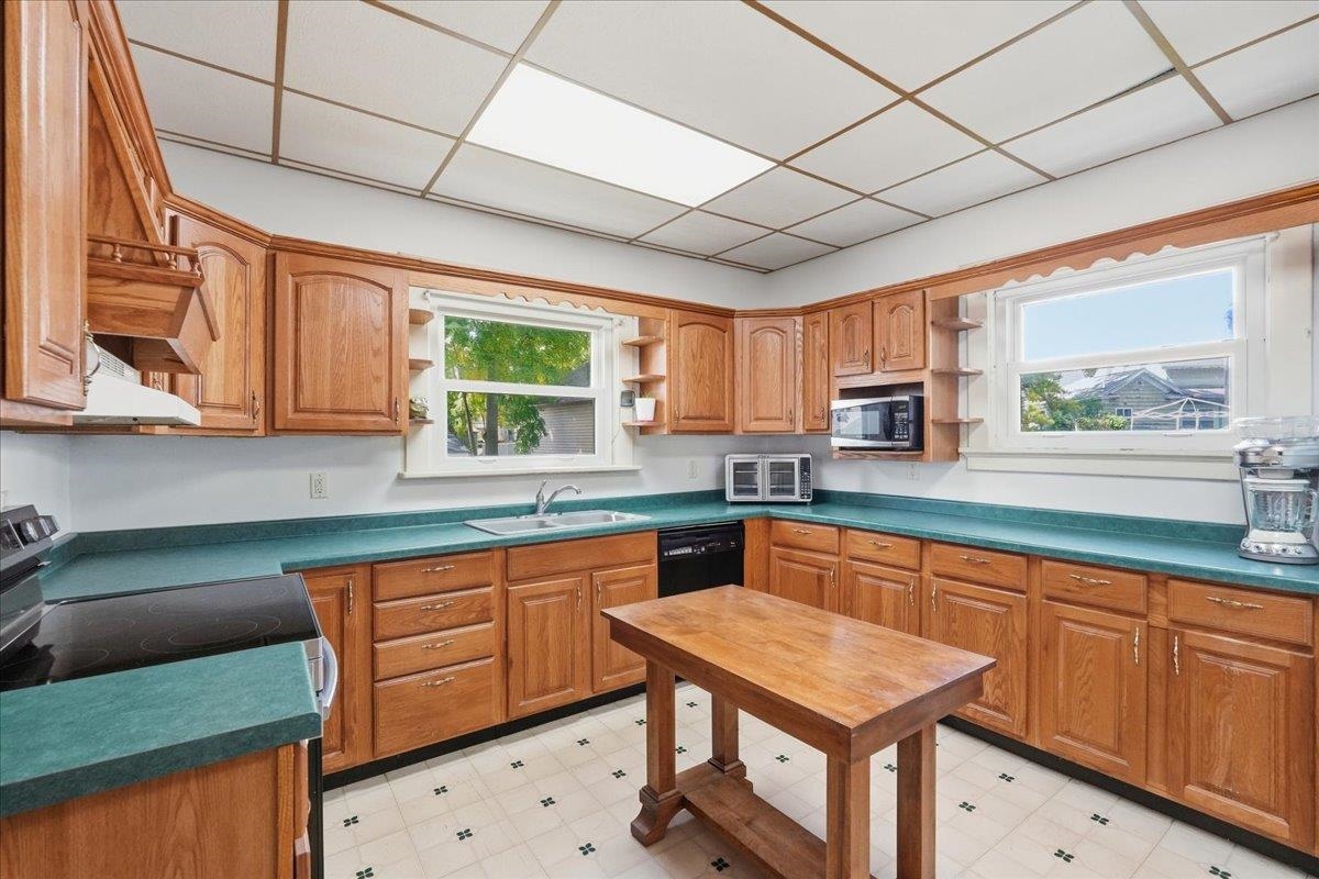 Kitchen with warm wood cabinets, teal countertops, a central table, and large windows.