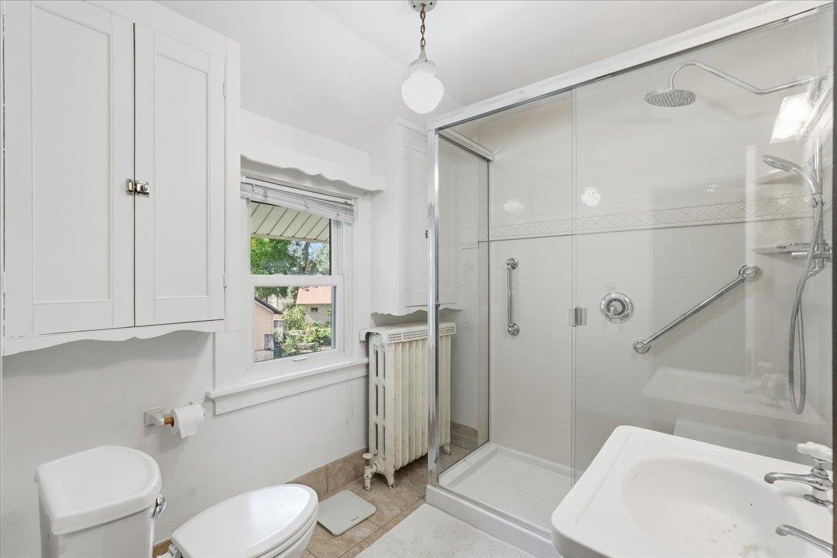 Bright bathroom with a glass-enclosed shower, built-in cabinets, and a window above a vintage radiator.