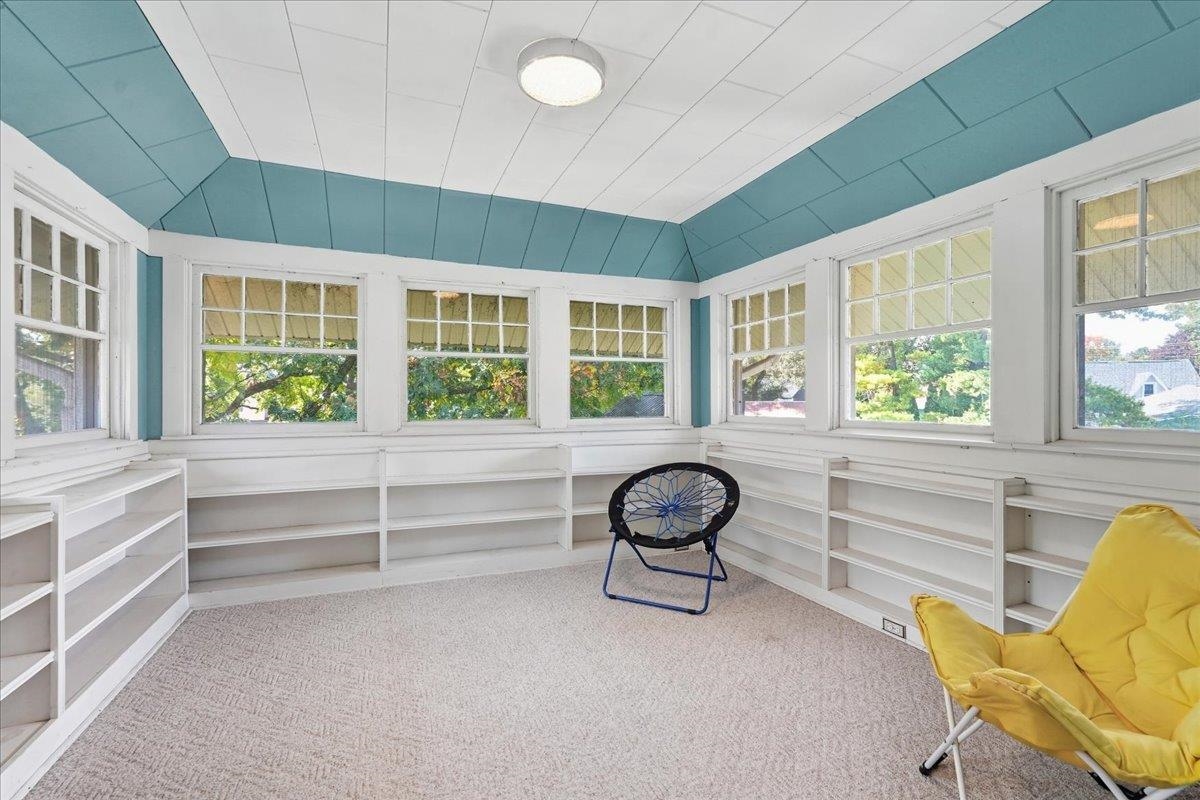Sunroom with wraparound windows, built-in shelves, and a distinctive teal paneled ceiling.