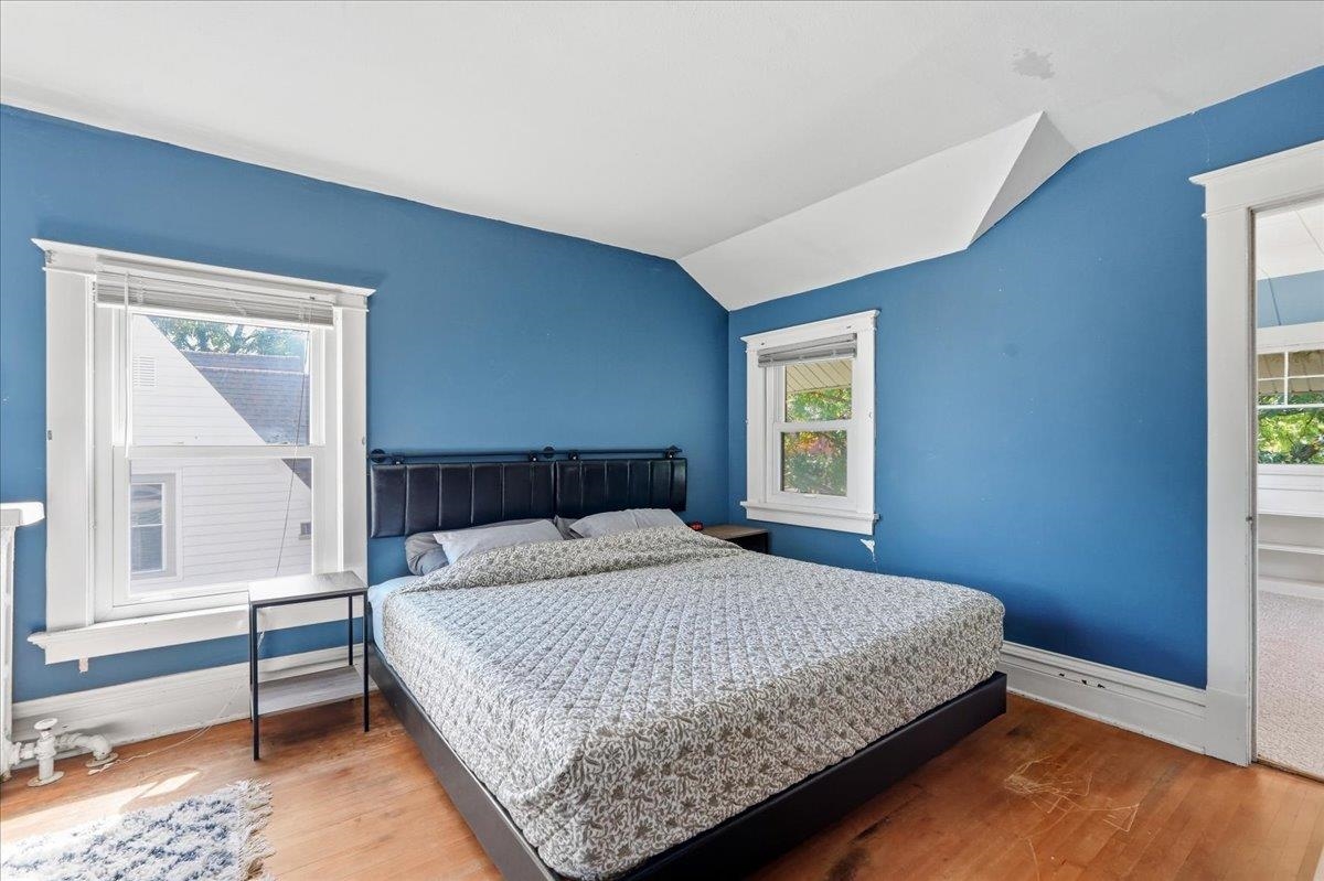Bedroom with blue walls, white-trimmed windows, wood flooring, and a large bed.