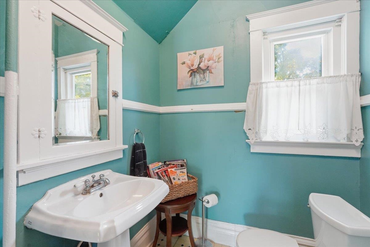 Turquoise bathroom with a pedestal sink, mirrored cabinet, curtained window, and toilet.