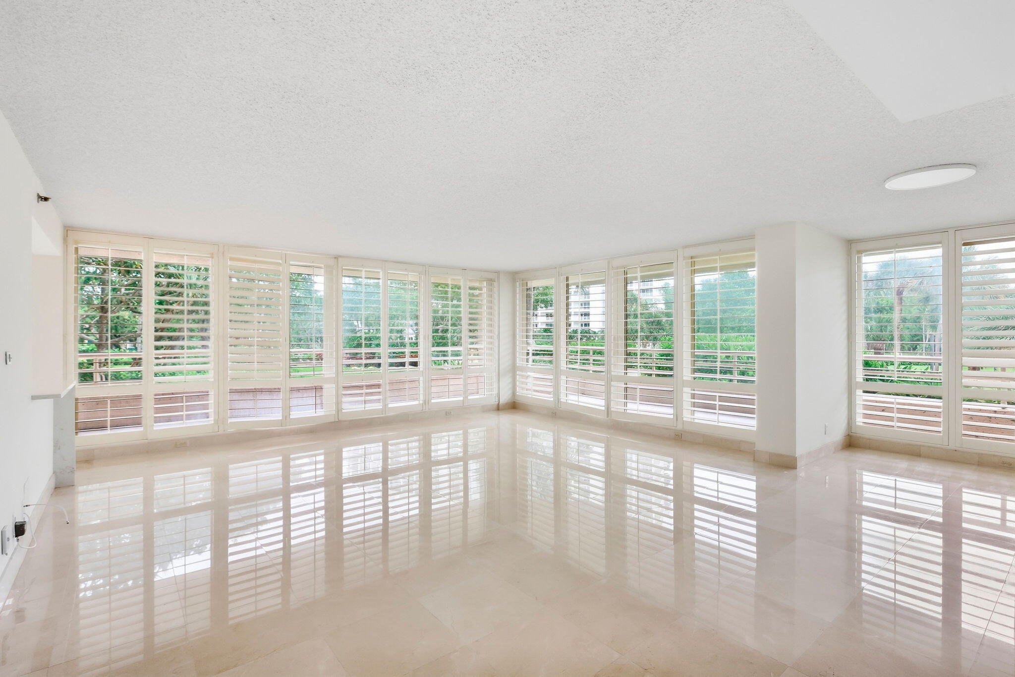 Vacant living room with glossy tile floors and wide plantation-shuttered windows.