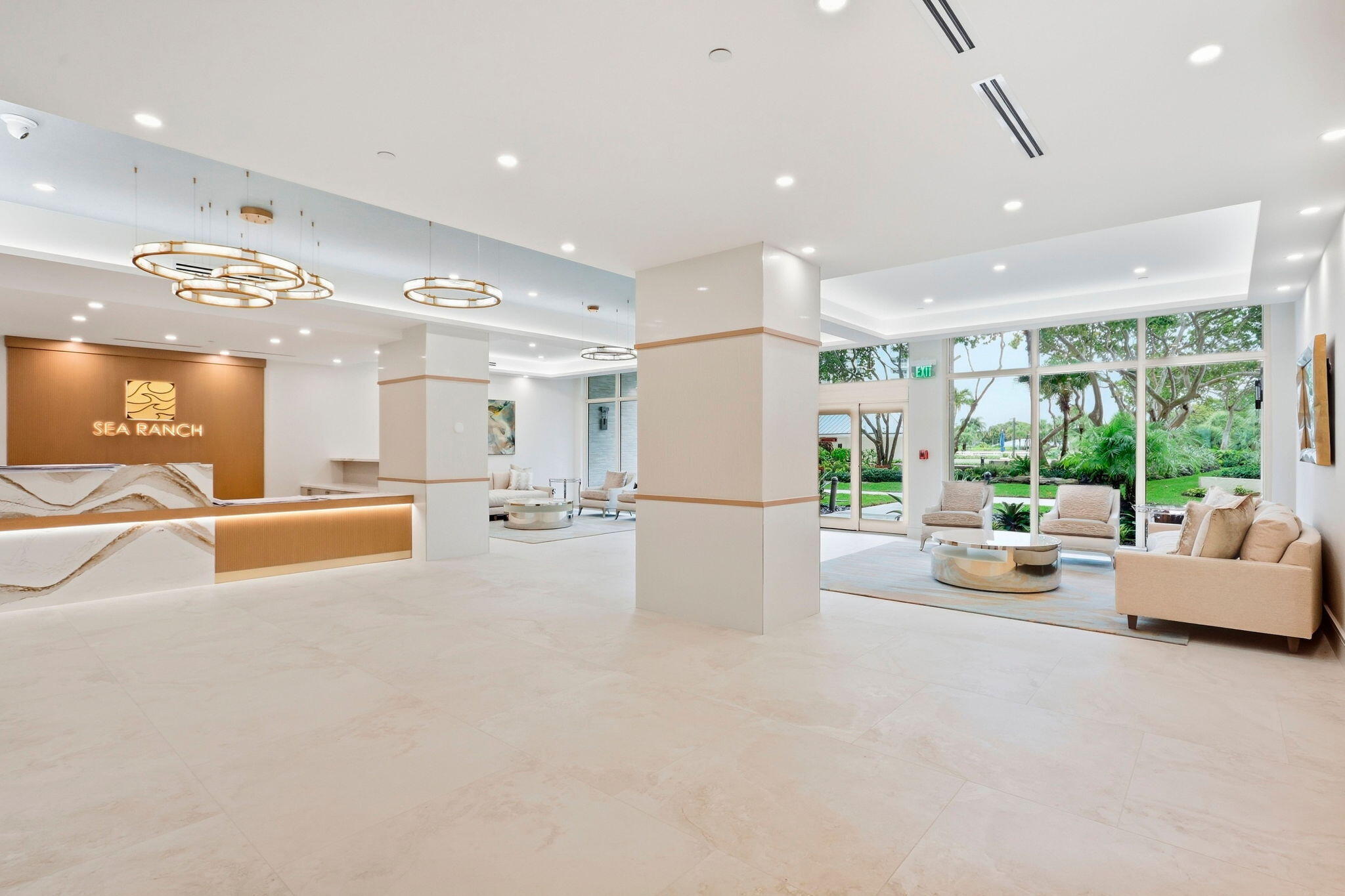 Sea Ranch lobby with marble reception desk, modern pendant lights, and seating beside garden-facing windows.