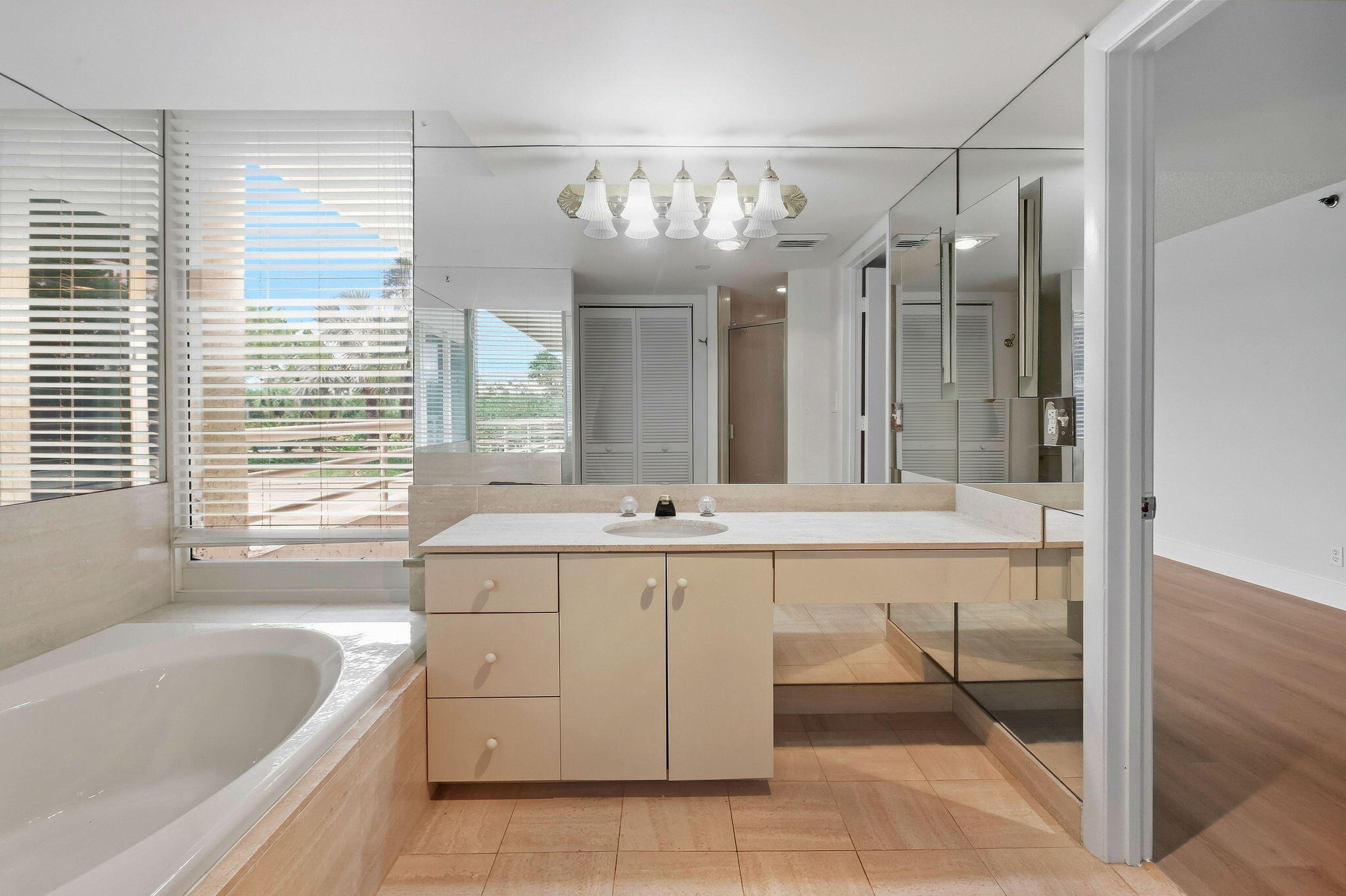 Bathroom with a soaking tub, mirrored vanity, and large windows with white blinds.