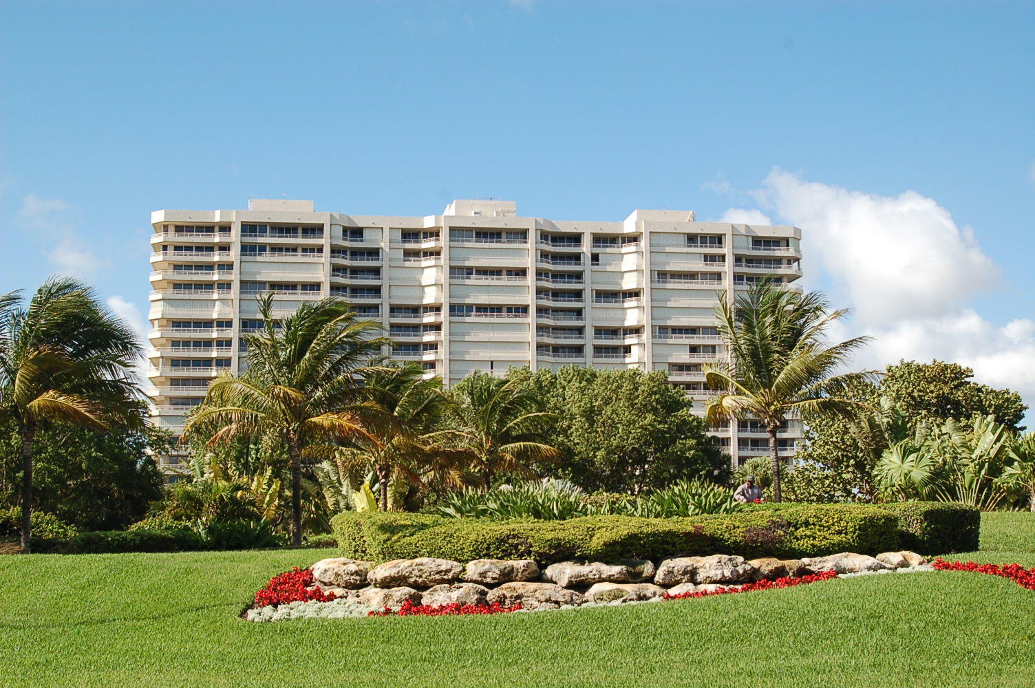 White condominium building behind palm trees and landscaped gardens.