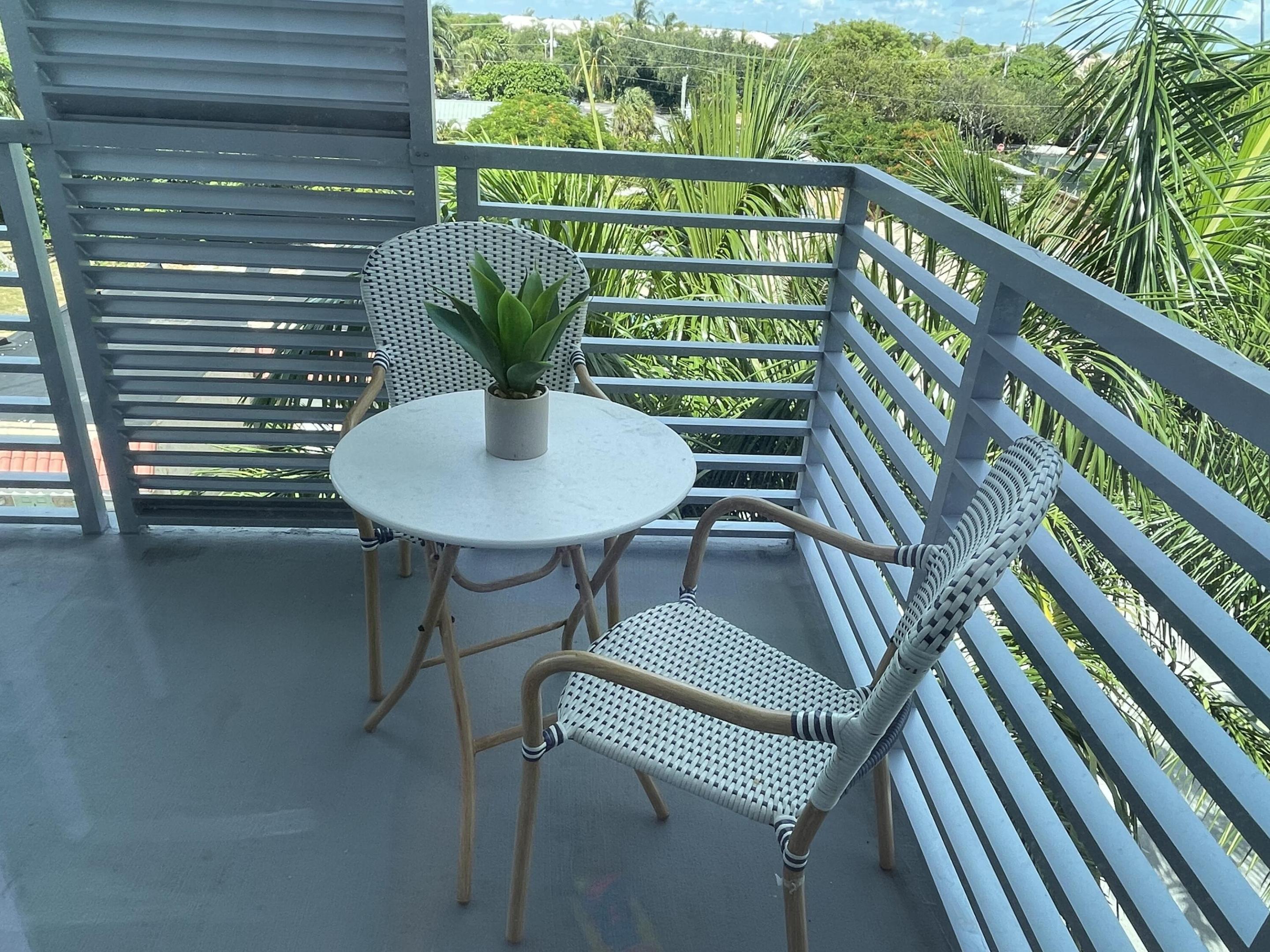 Furnished balcony with woven chairs and a table overlooking lush tropical greenery.