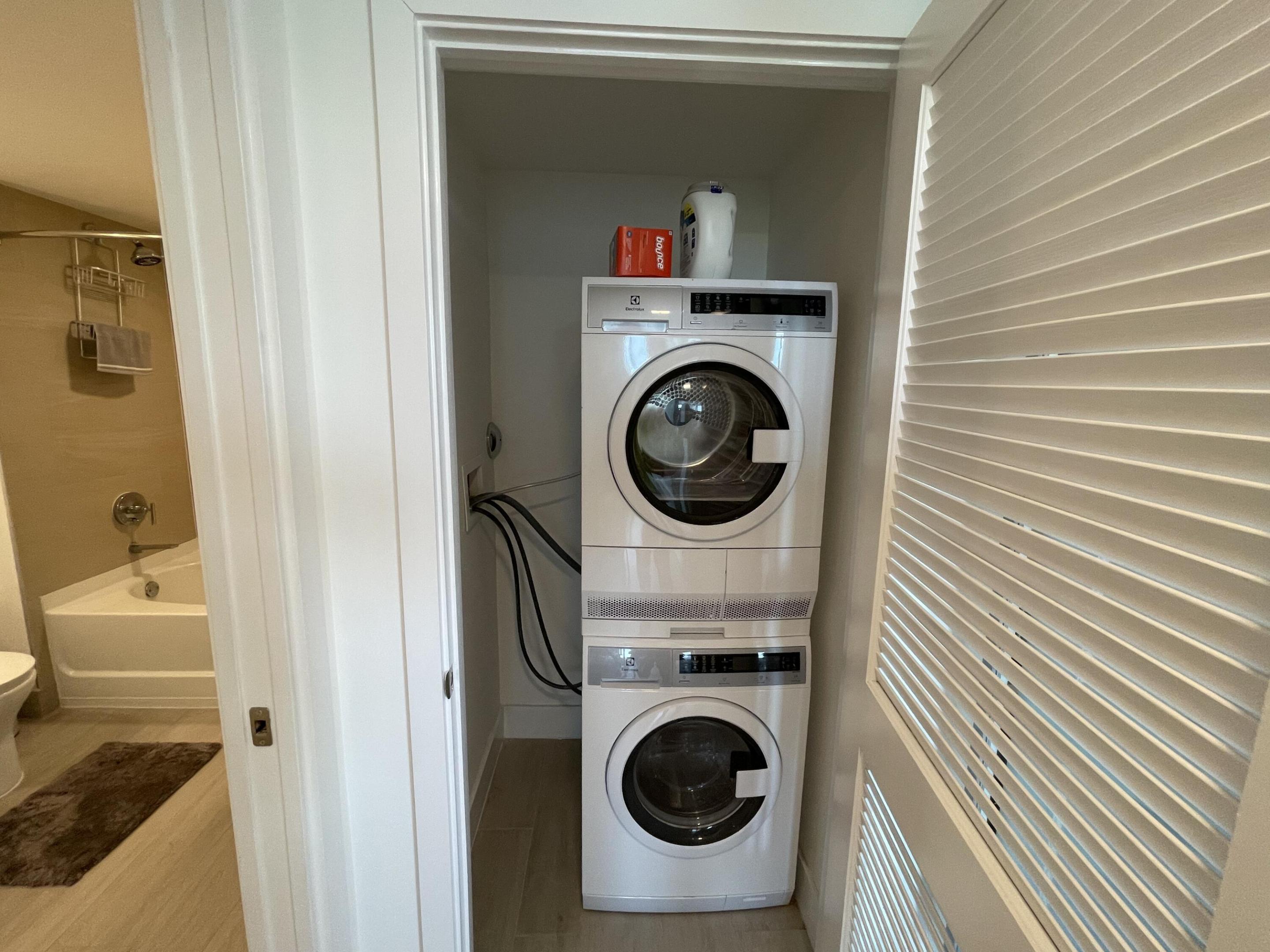 Laundry closet with stacked front-loading washer and dryer beside an open bathroom doorway.