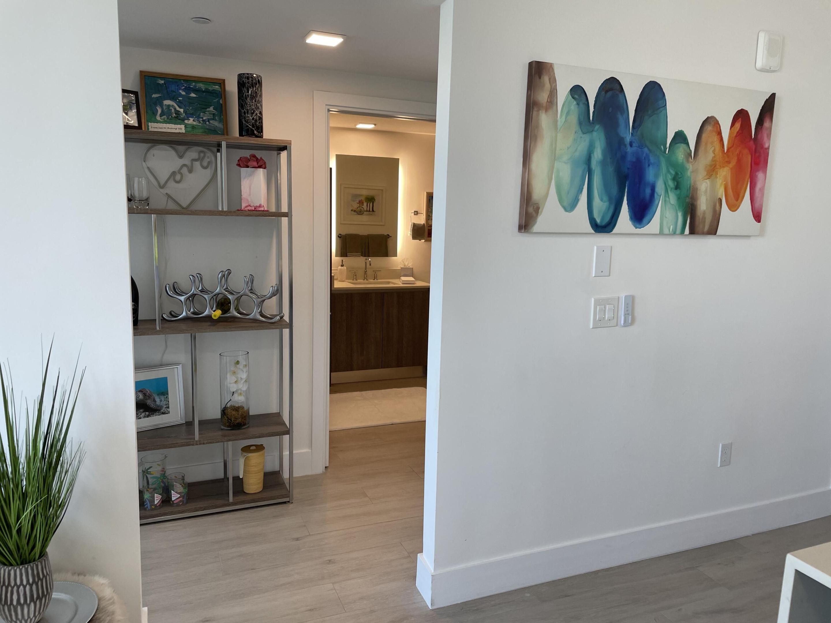 Furnished interior with a display shelf, colorful abstract wall art, and a bathroom vanity visible through the doorway.