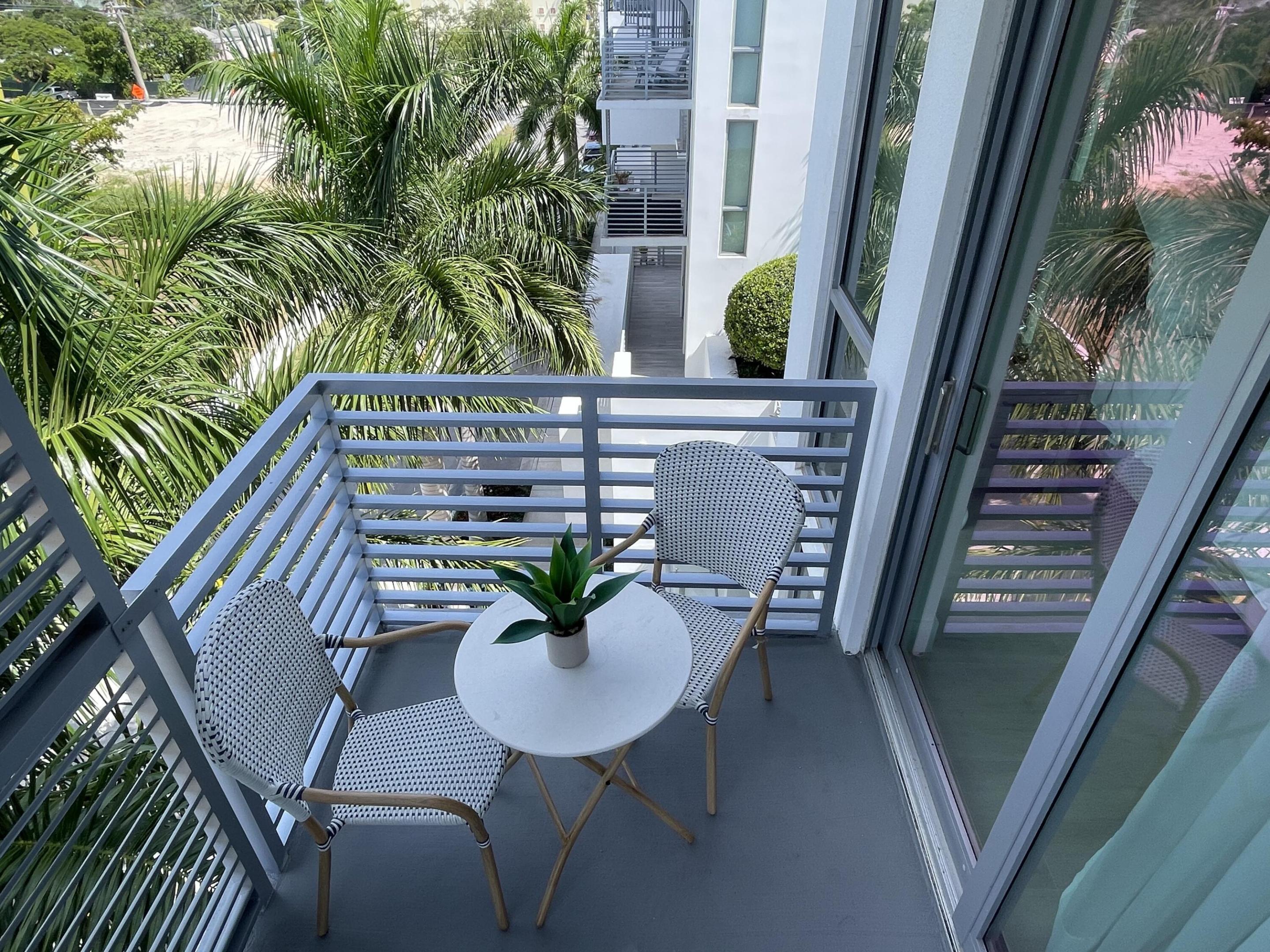 Furnished apartment balcony with woven chairs and a round table, surrounded by palm trees.