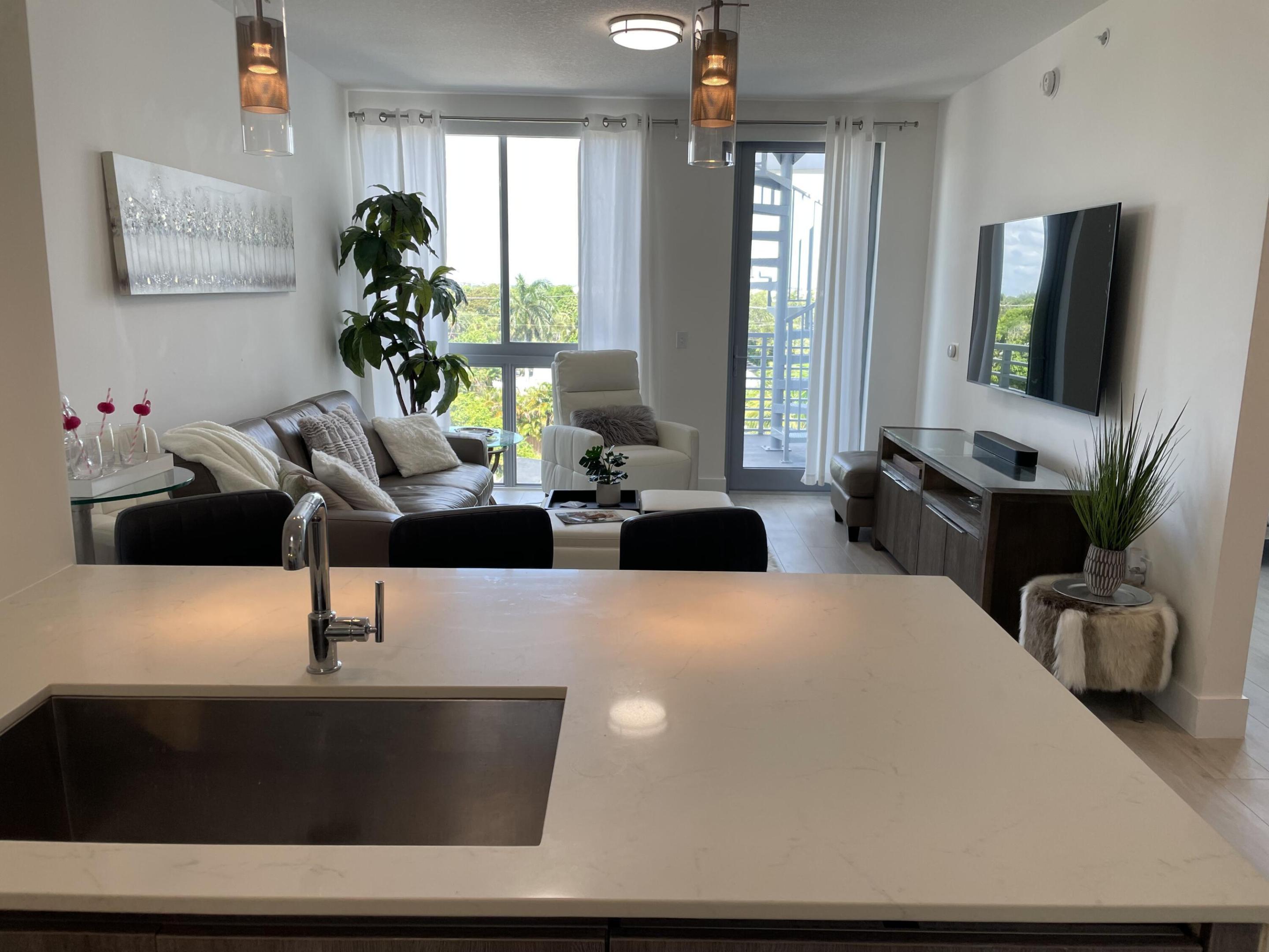 Condo living room with leather sofa, wall-mounted TV, and balcony windows, seen across a kitchen island.
