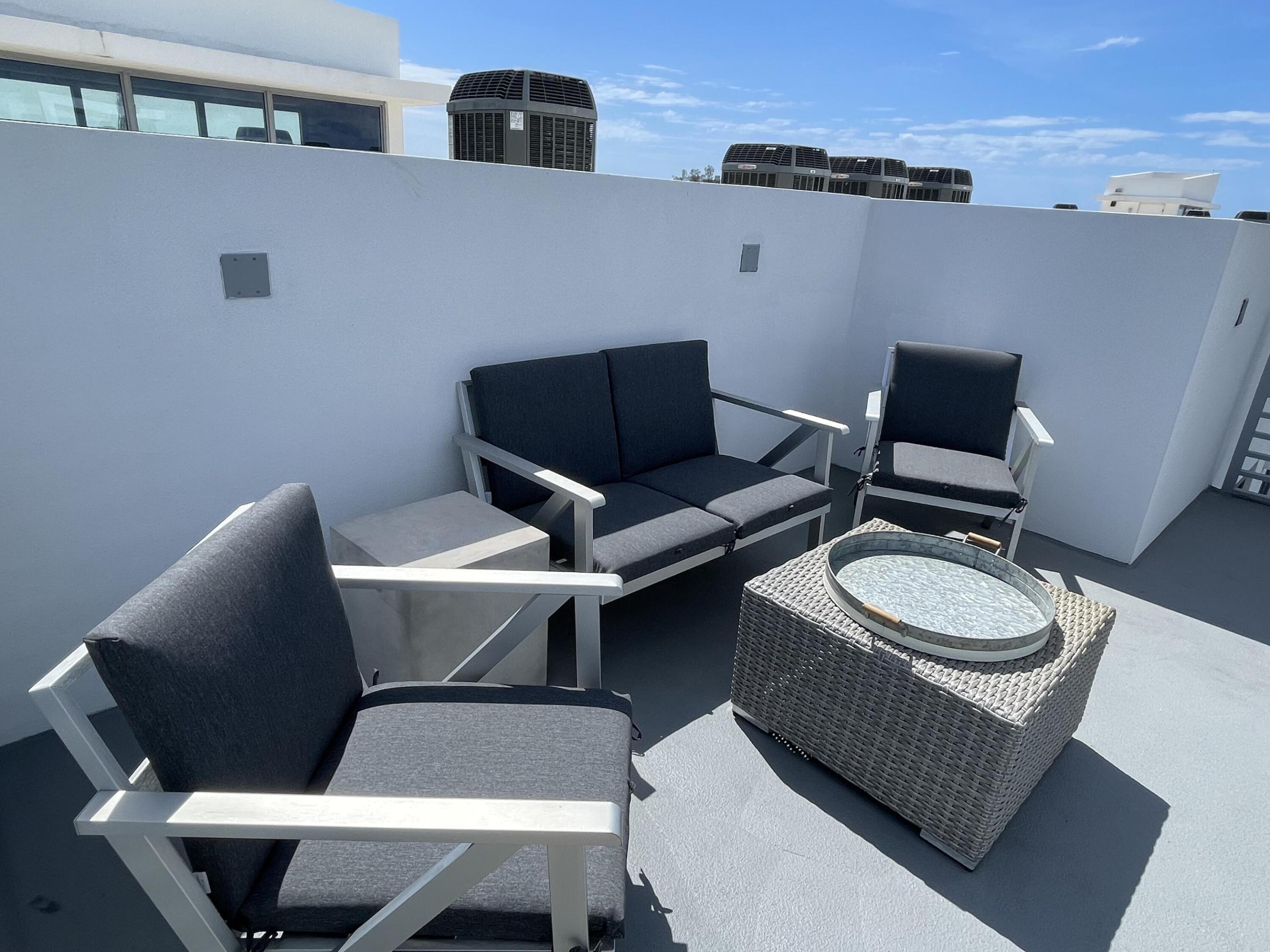 Rooftop terrace seating with three cushioned chairs and a woven coffee table in bright sunlight.