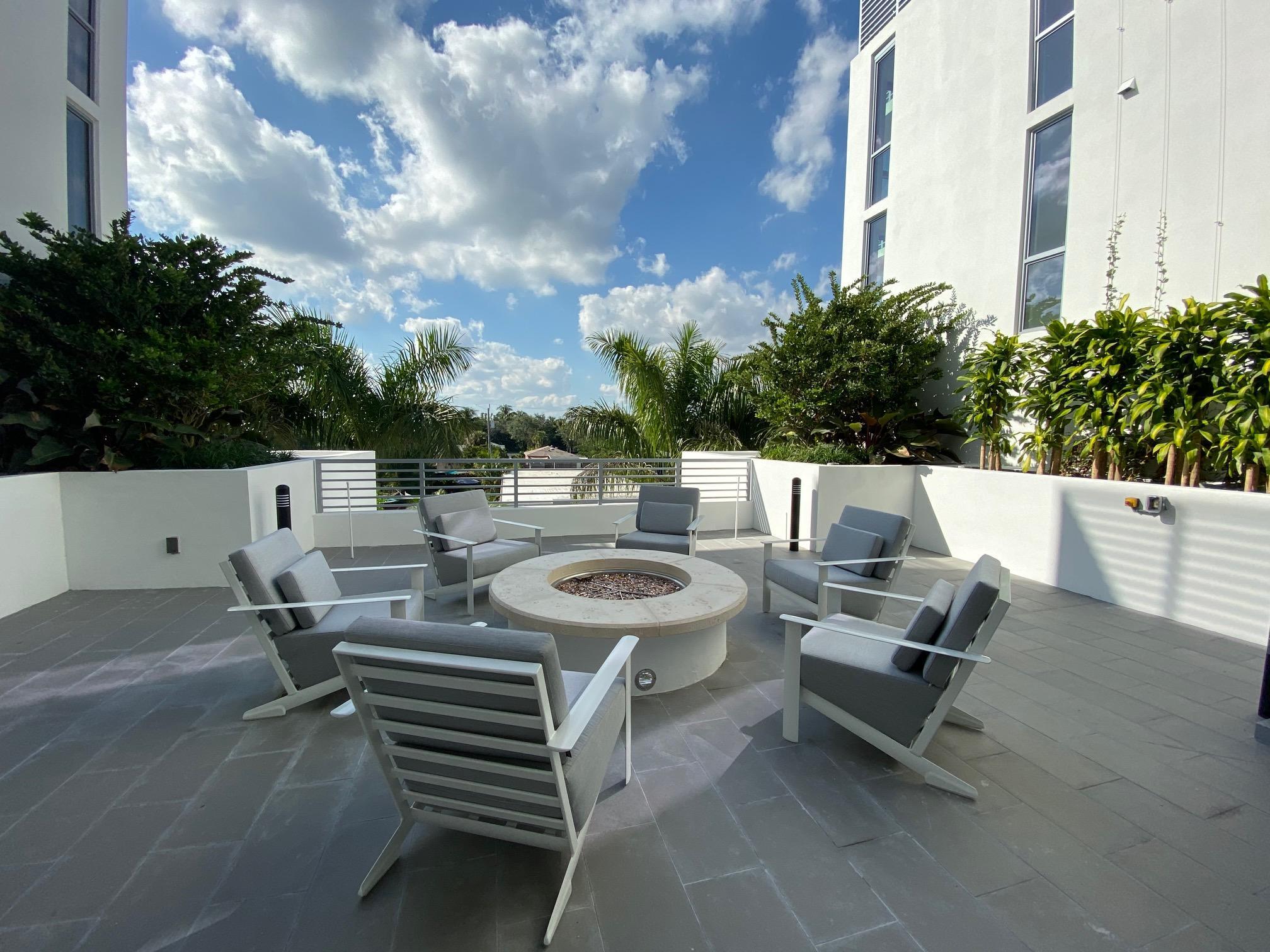 Outdoor terrace with lounge chairs around a circular fire pit and tropical landscaping.