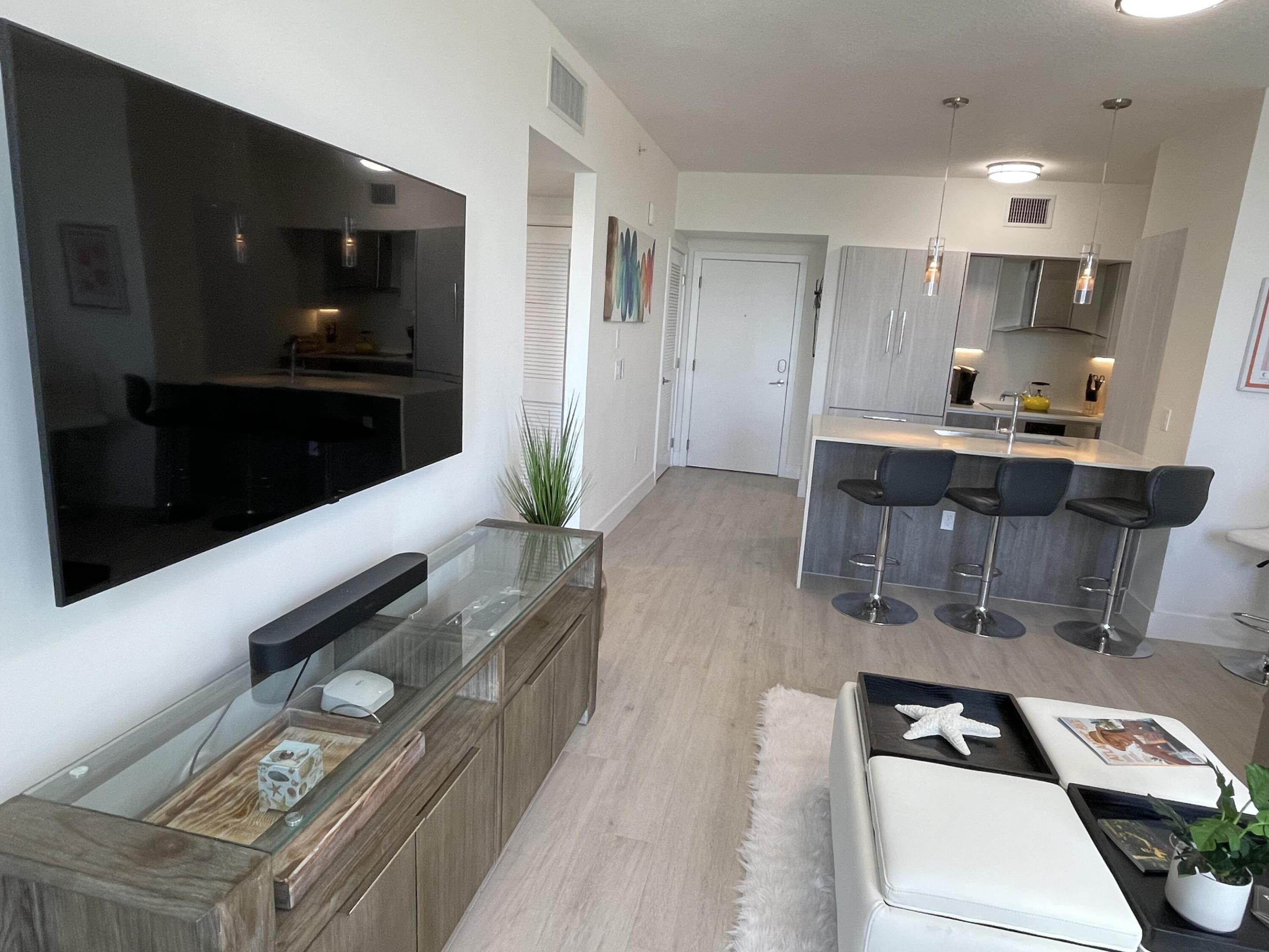 Furnished condo living room opening to a kitchen with a gray island and three bar stools.