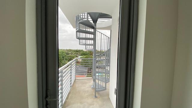 Balcony with metal railings and a gray spiral staircase overlooking treetops.