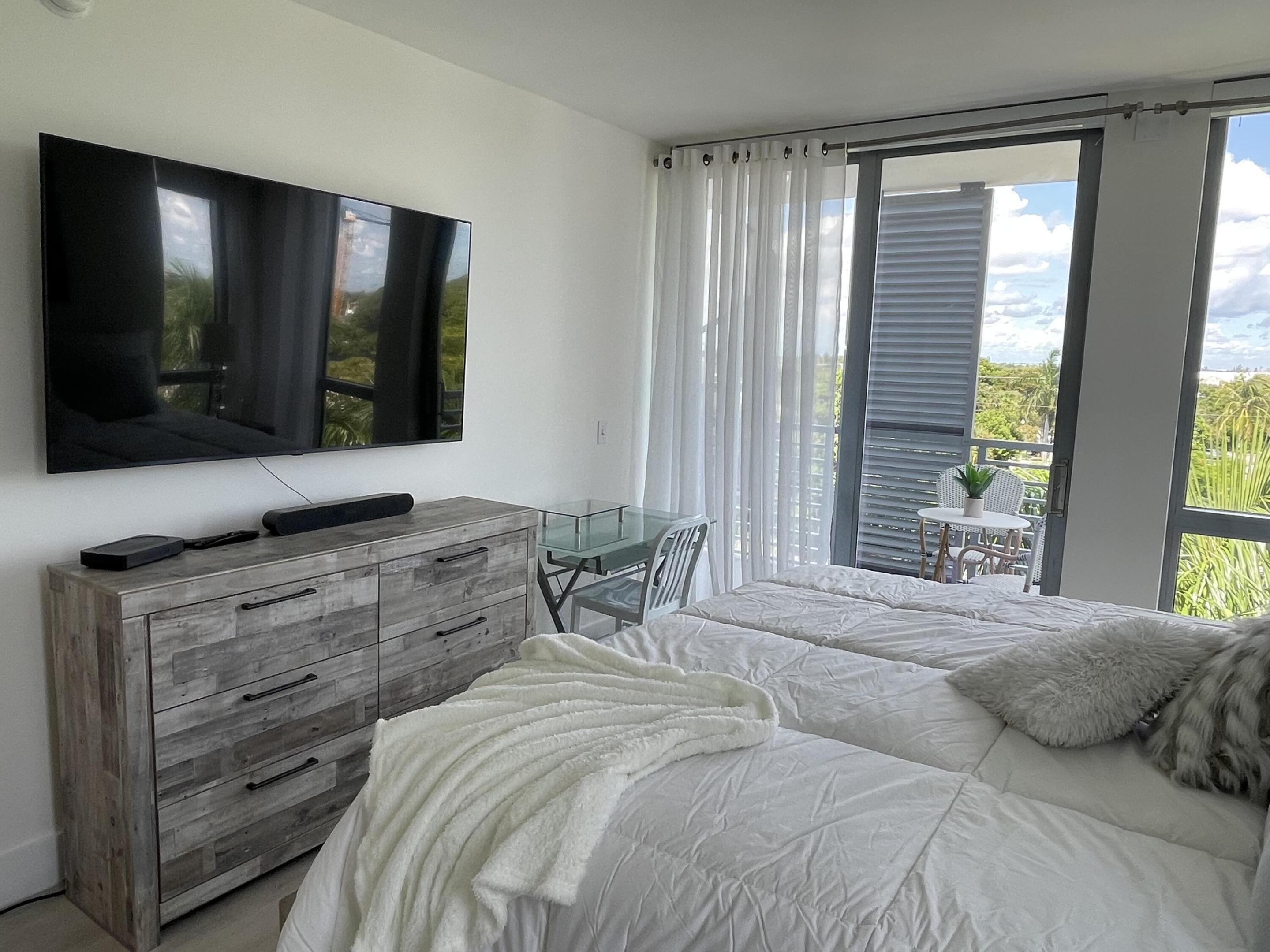 Bedroom with a white bed and sliding doors opening to a balcony overlooking palm trees.