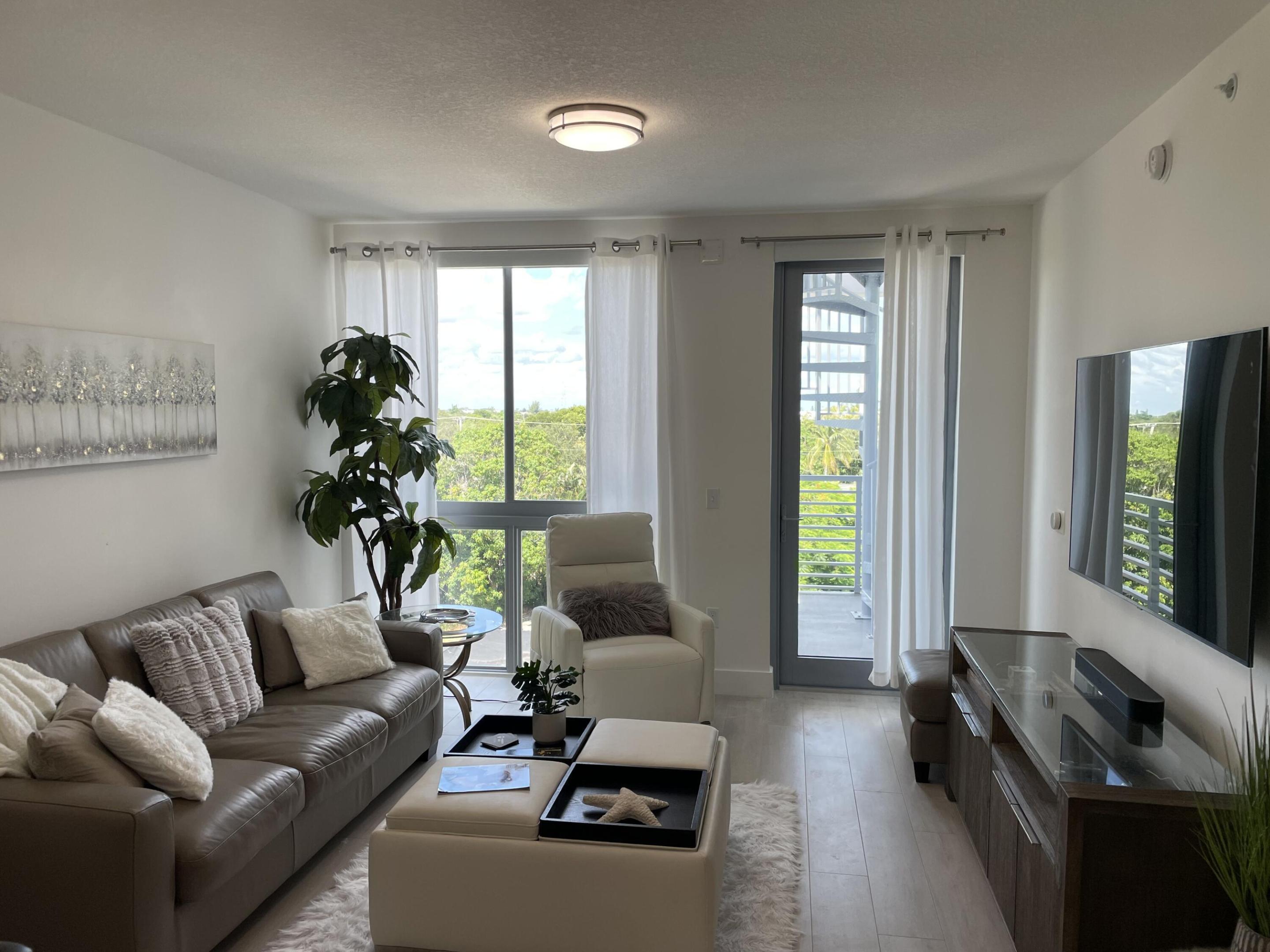 Living room with a gray sectional, cream armchair, and sliding doors to a balcony overlooking trees.
