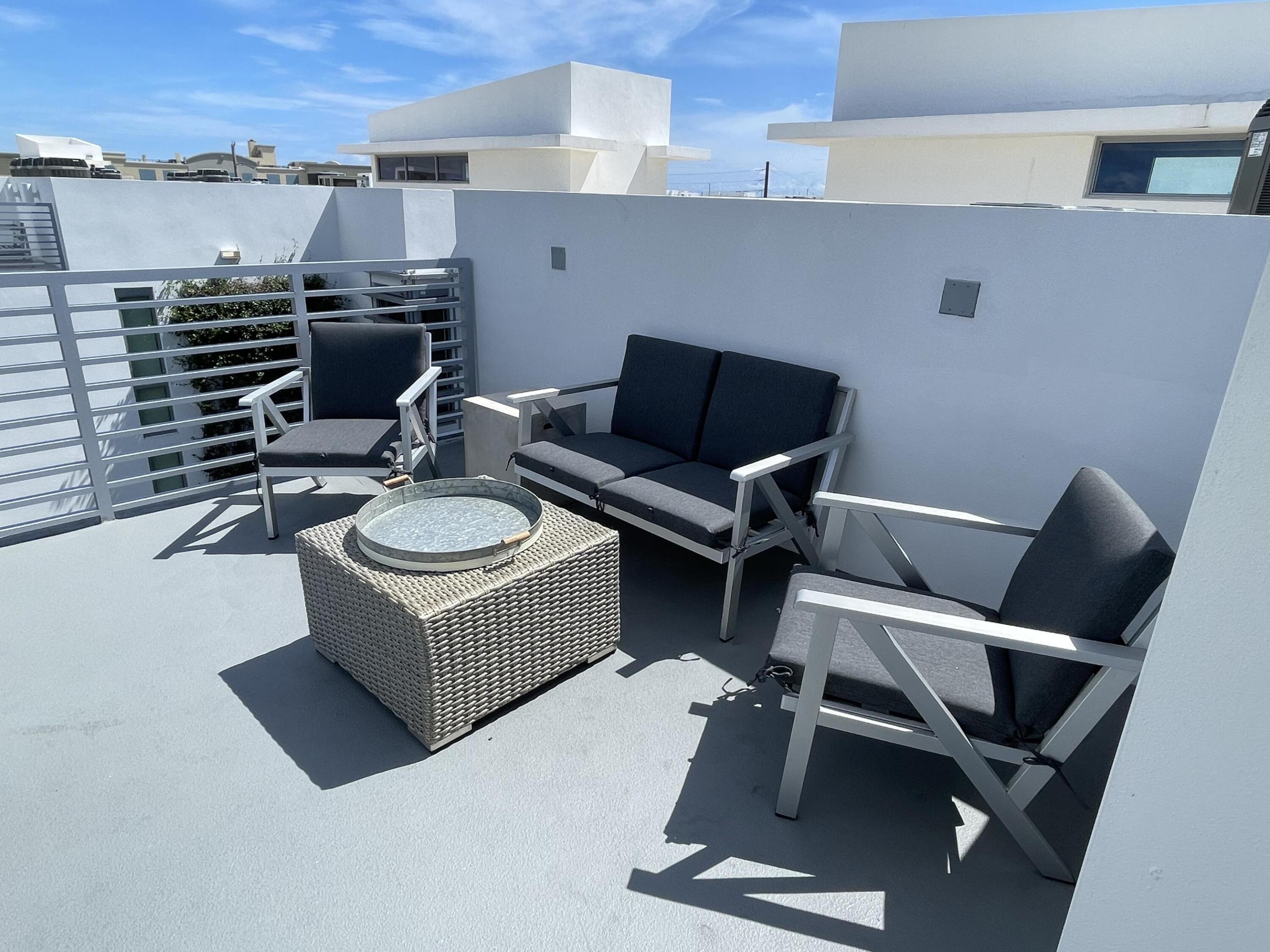 Rooftop terrace with dark outdoor seating, a woven coffee table, and white privacy walls.