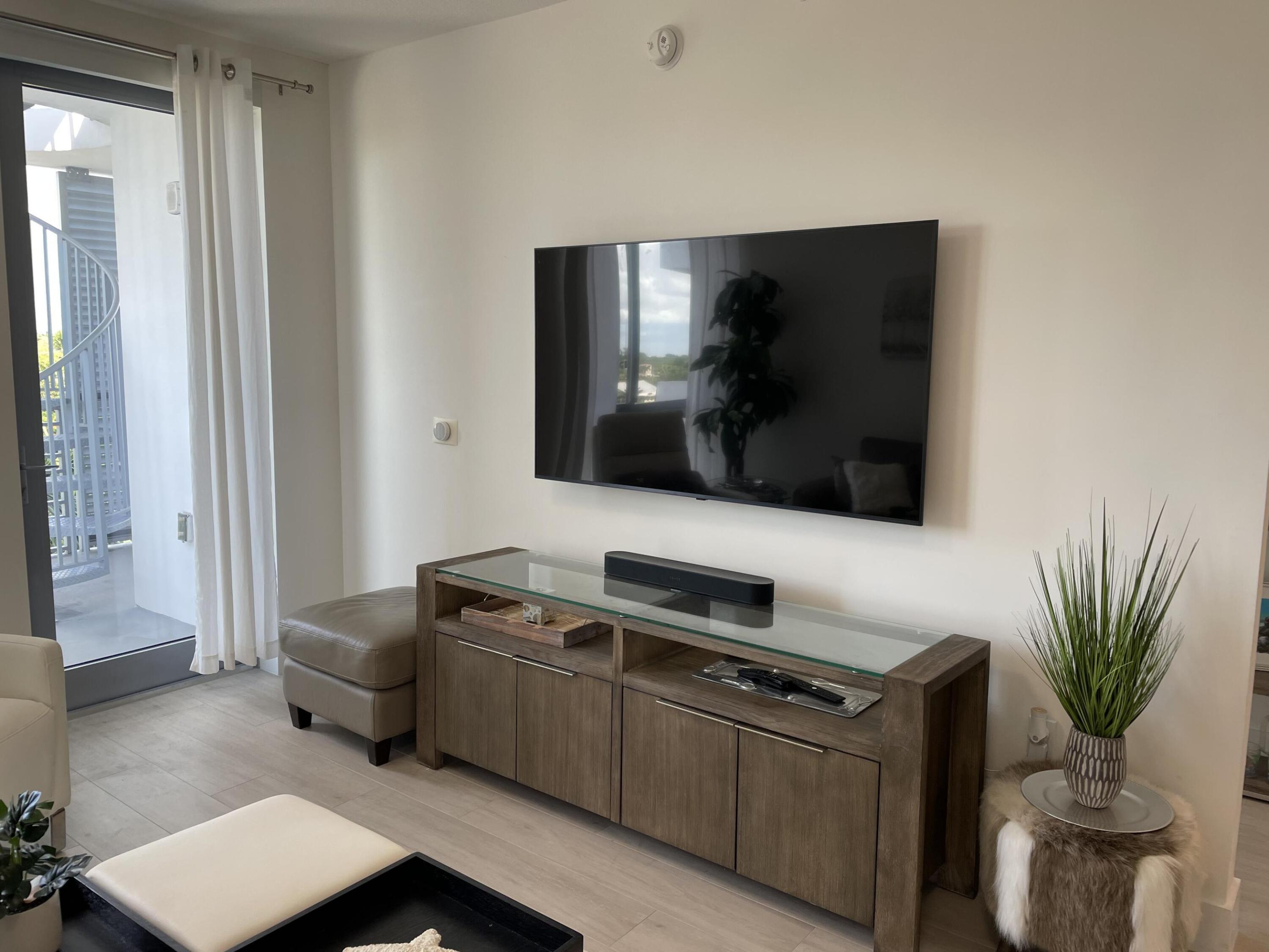 Living room with a wall-mounted television, wood media console, and balcony access.