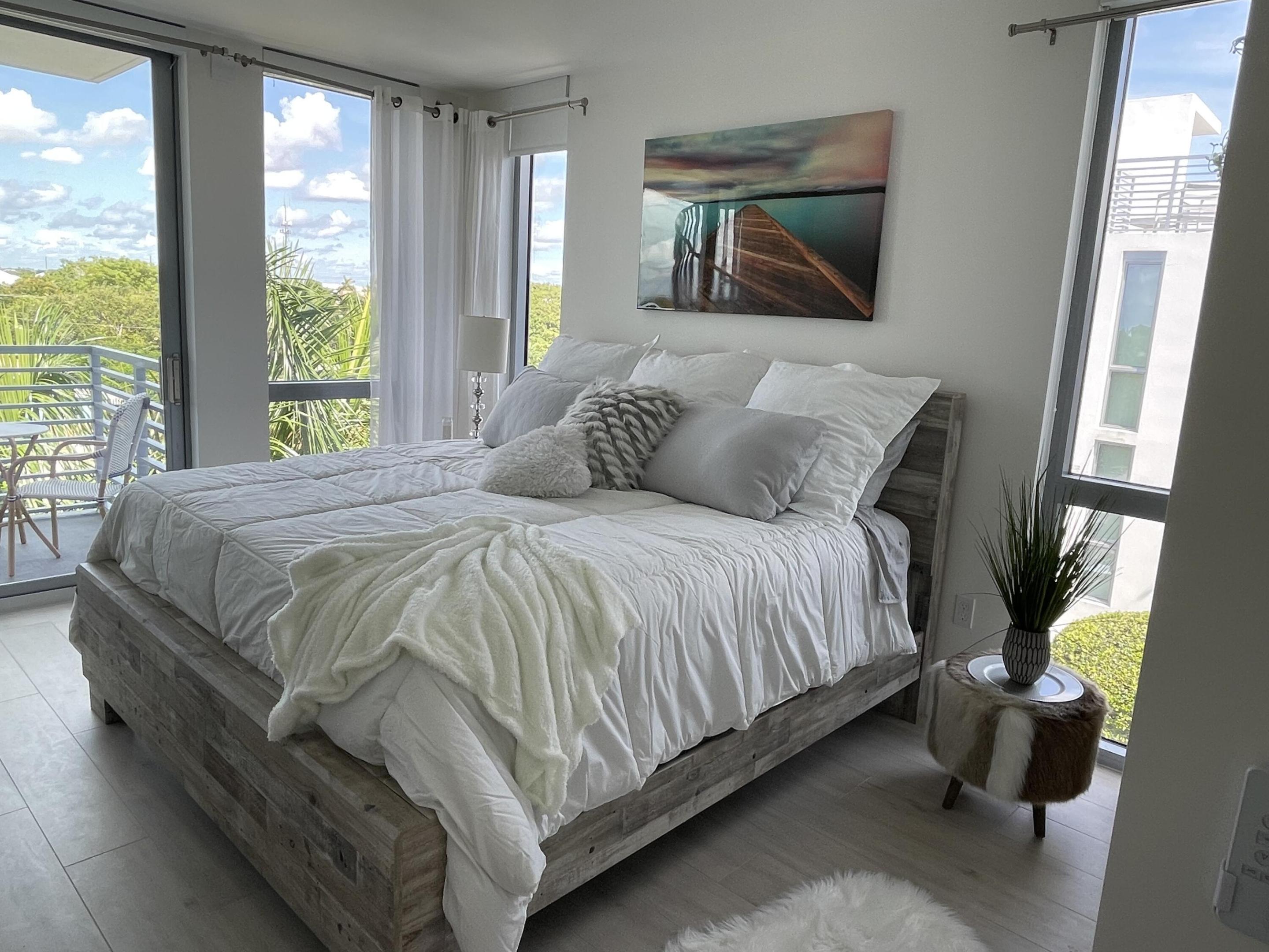 Bedroom with a gray wood platform bed, white bedding, and floor-to-ceiling windows opening onto a balcony.