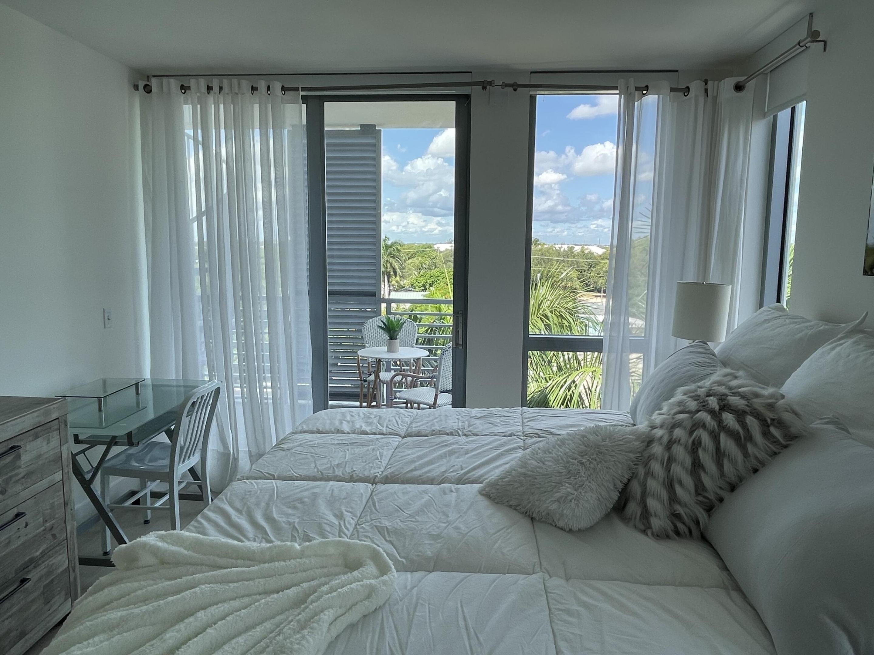 Bedroom with a white bed and balcony doors overlooking leafy greenery.