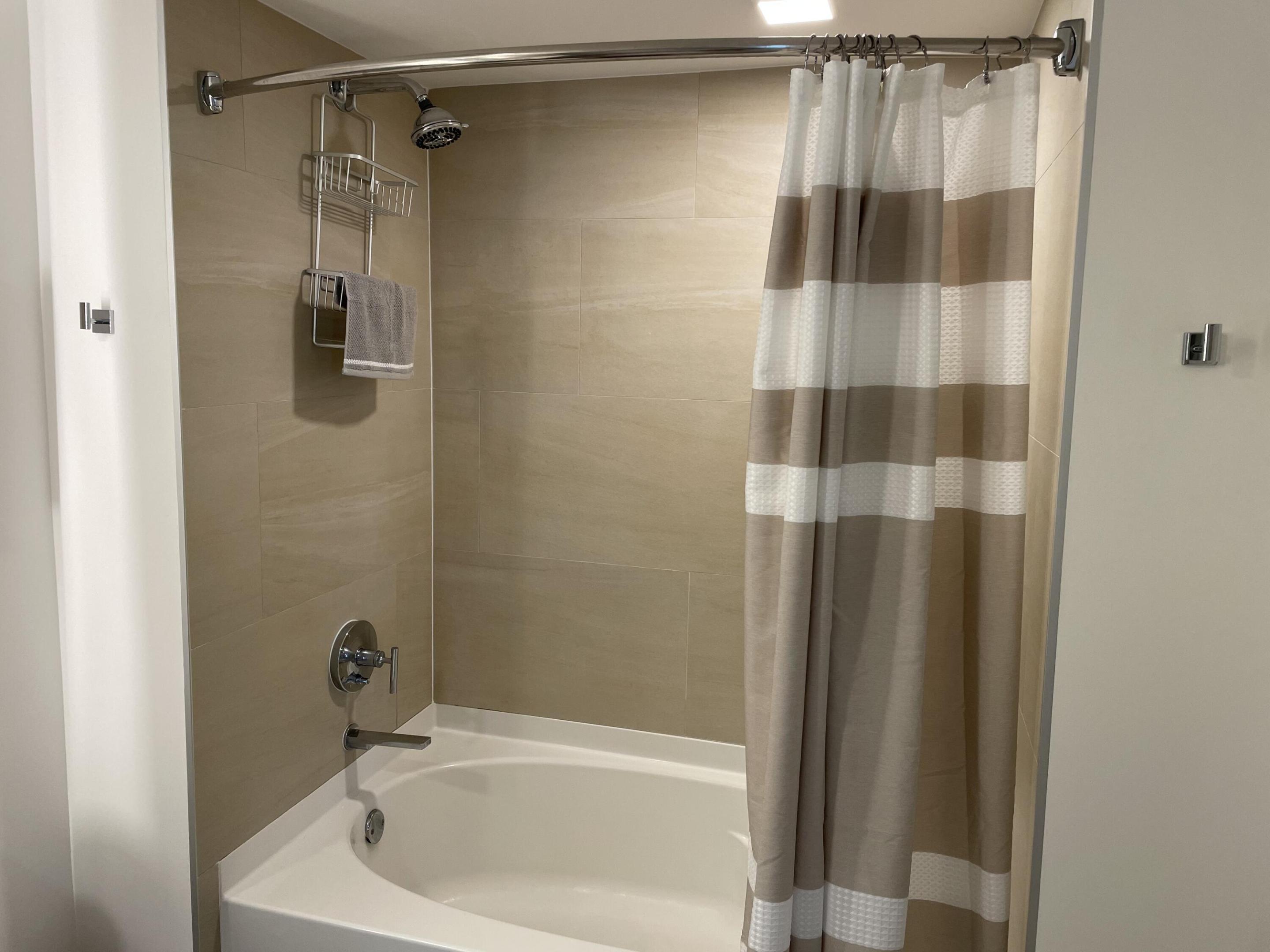 Tiled bathtub and shower with chrome fixtures and a gray-and-white striped curtain.