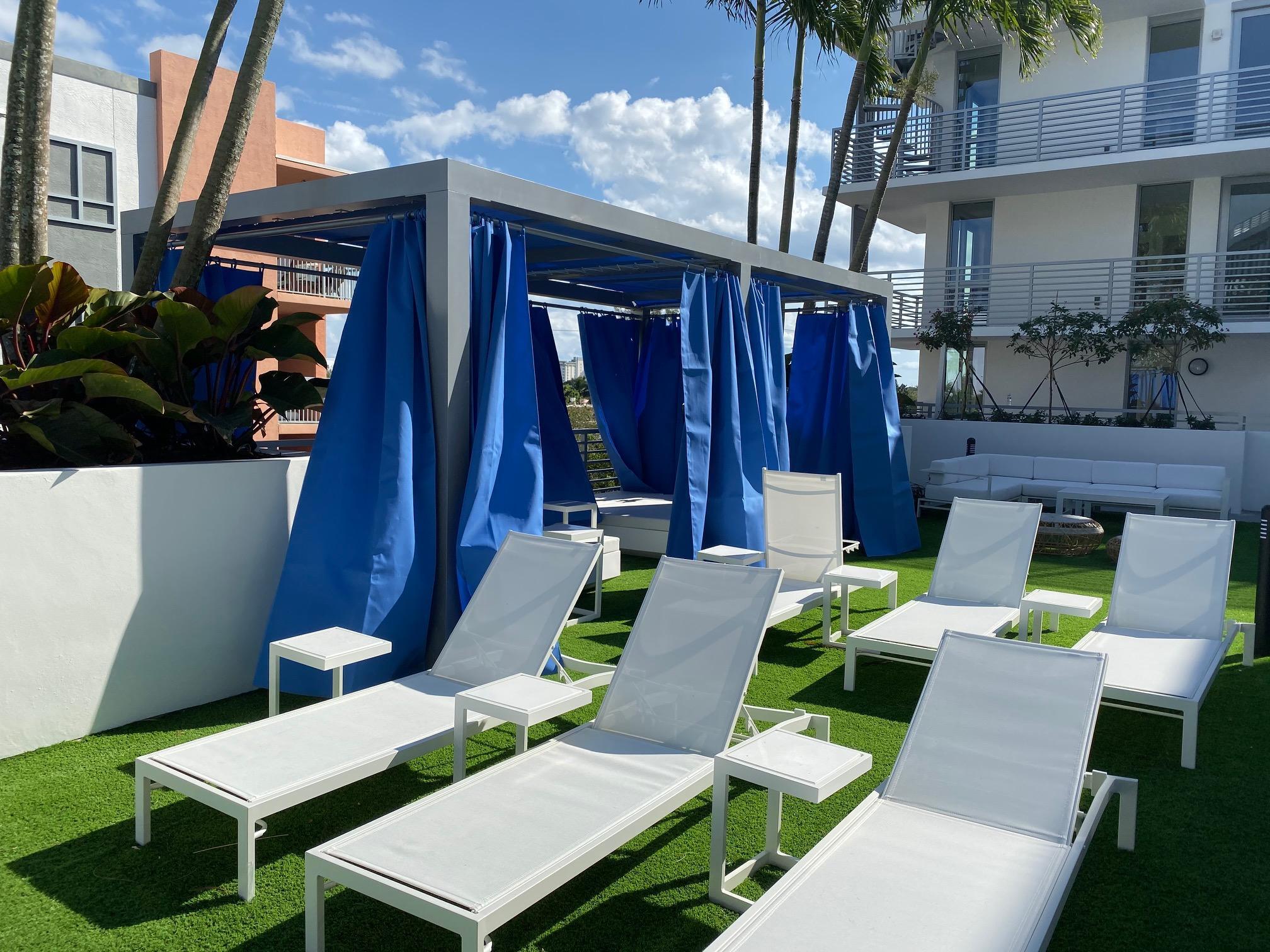 Condominium outdoor lounge with white chaise lounges and blue-curtained cabanas.