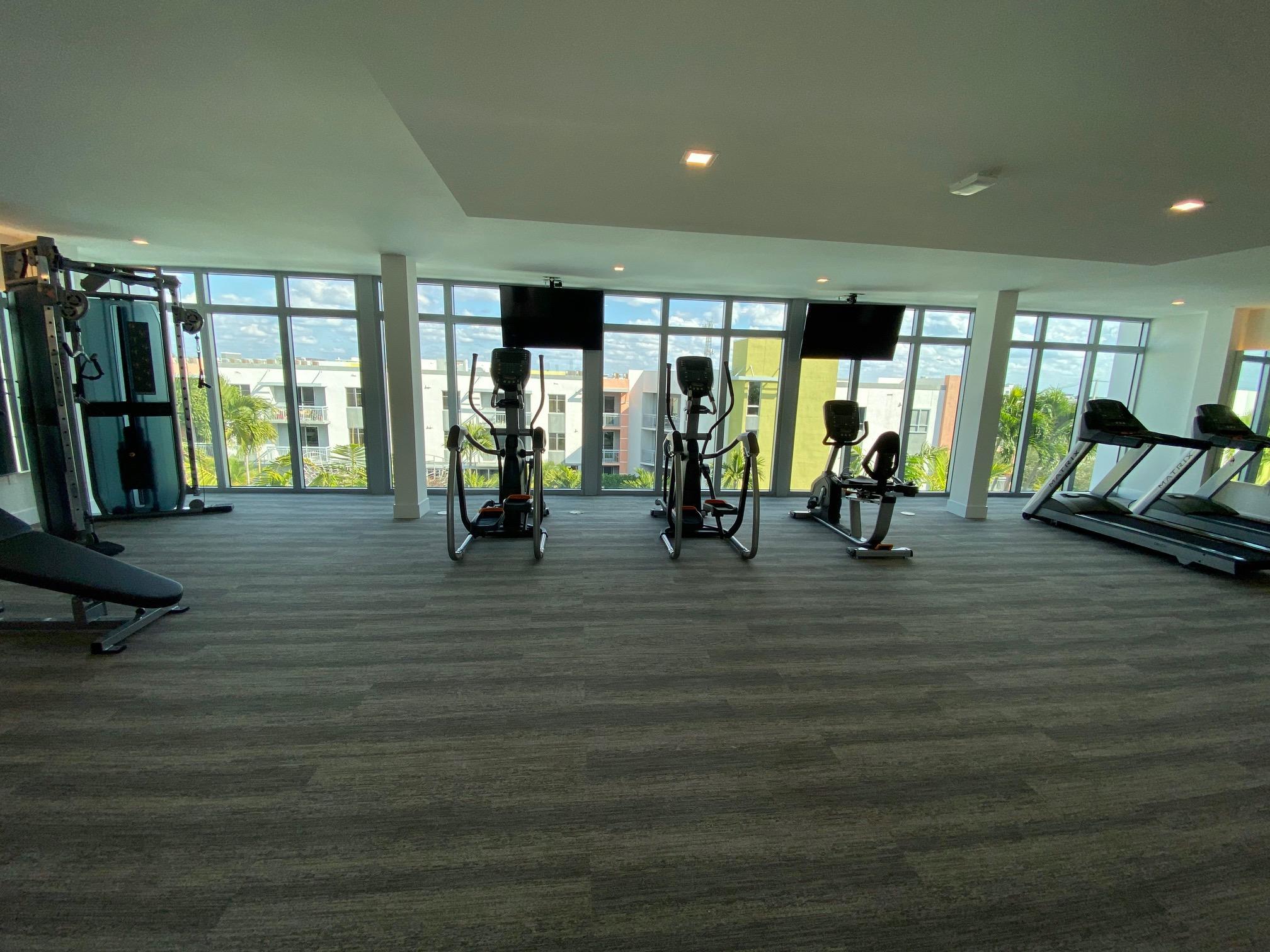 Condominium gym with treadmills, ellipticals, weight machines, and floor-to-ceiling windows.