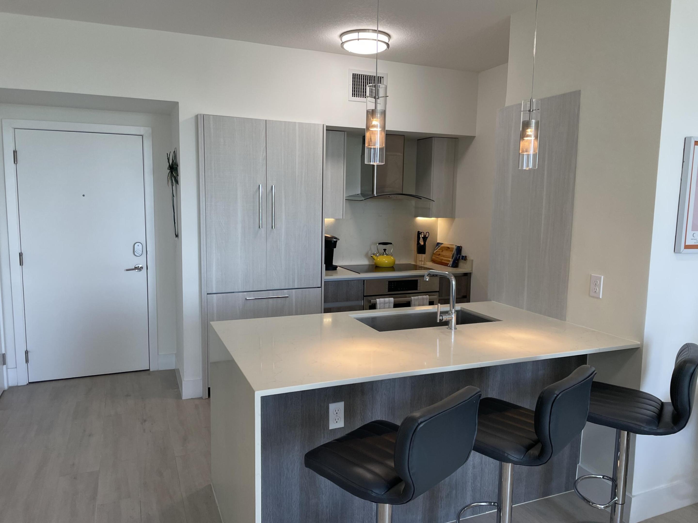 Modern condo kitchen with a large white island, sink, and three black bar stools.