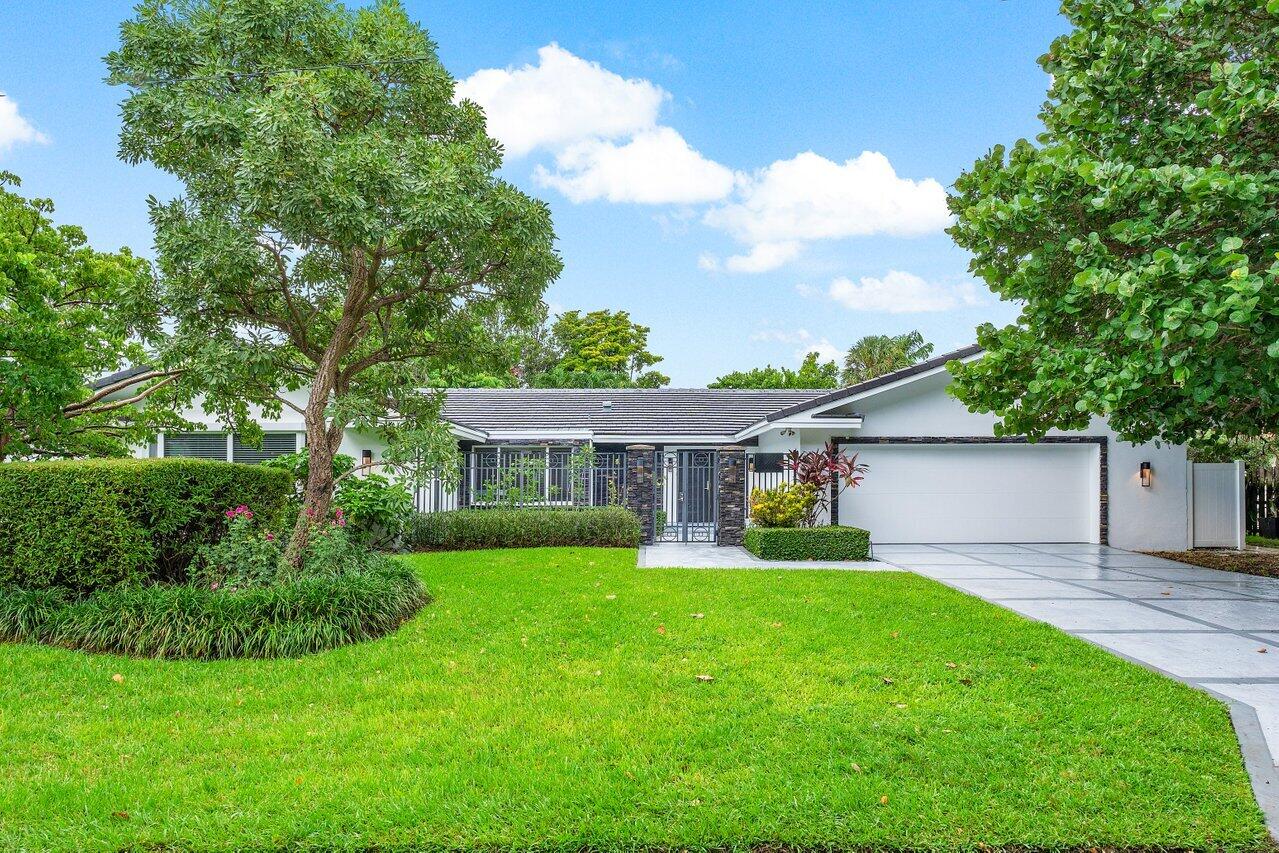 Modern white single-story home with a gated entry, attached garage, and broad green lawn.