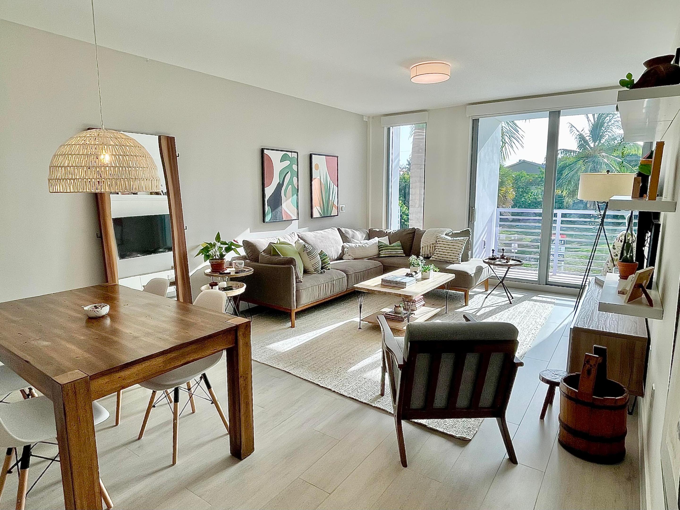 Furnished condo living and dining area with a sectional sofa and palm trees beyond the balcony.