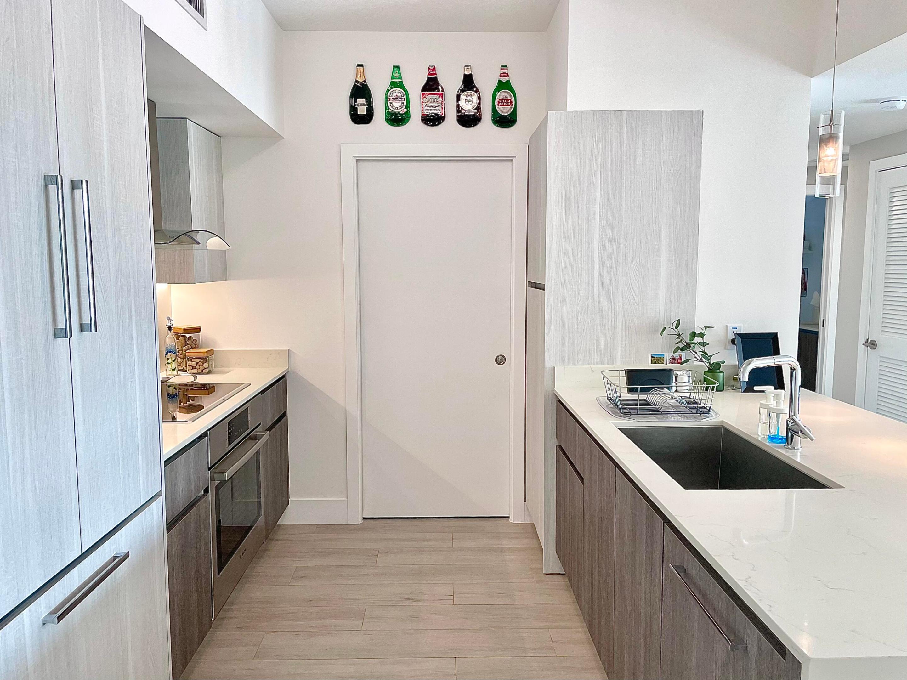 Modern galley kitchen with gray cabinetry, white counters, a large sink, and bottle-shaped wall decor.