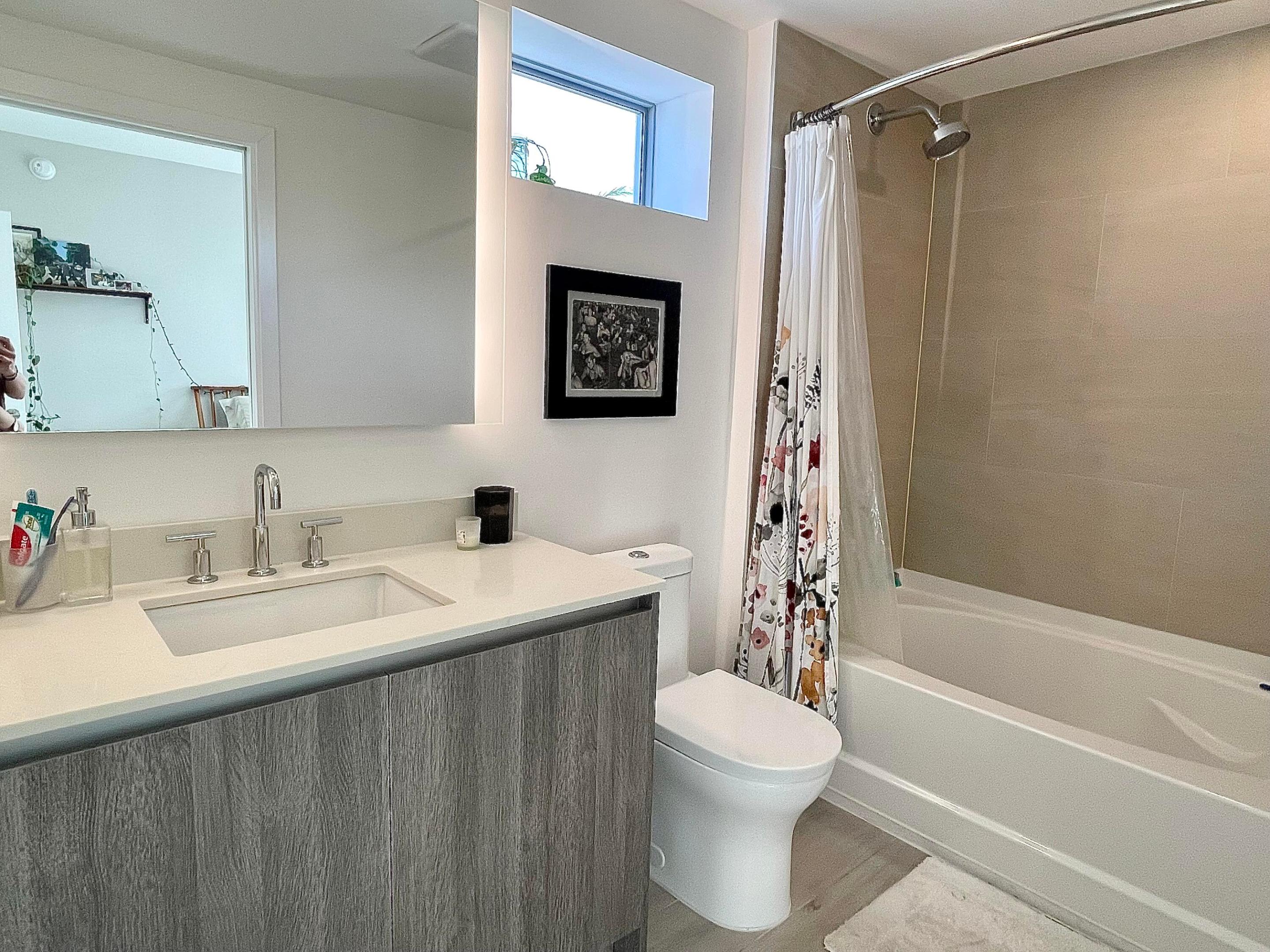 Bathroom with gray wood vanity, white sink, toilet, and bathtub with a floral shower curtain.