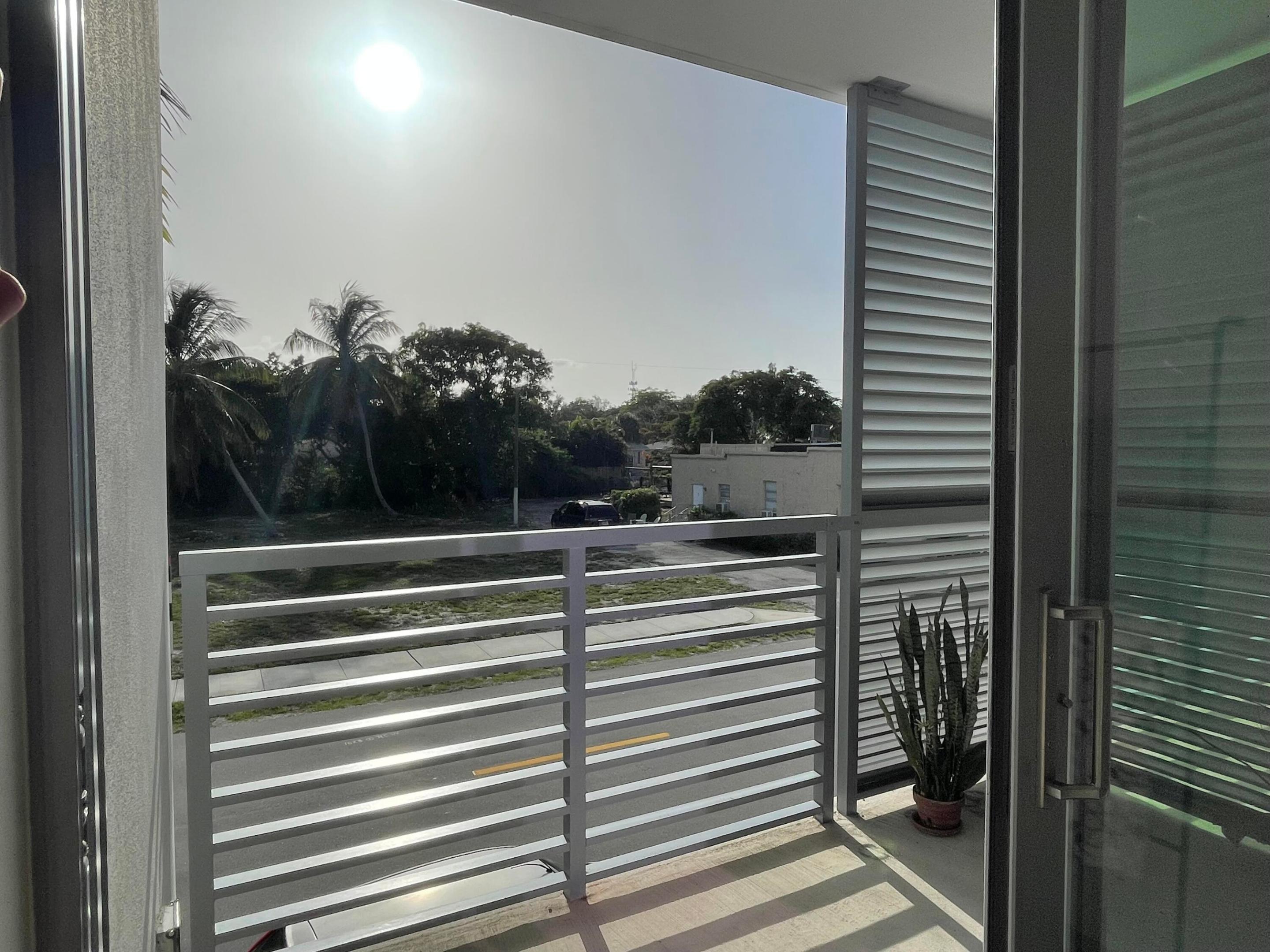 Condo balcony with metal railing and potted plant overlooking palm trees and a street.
