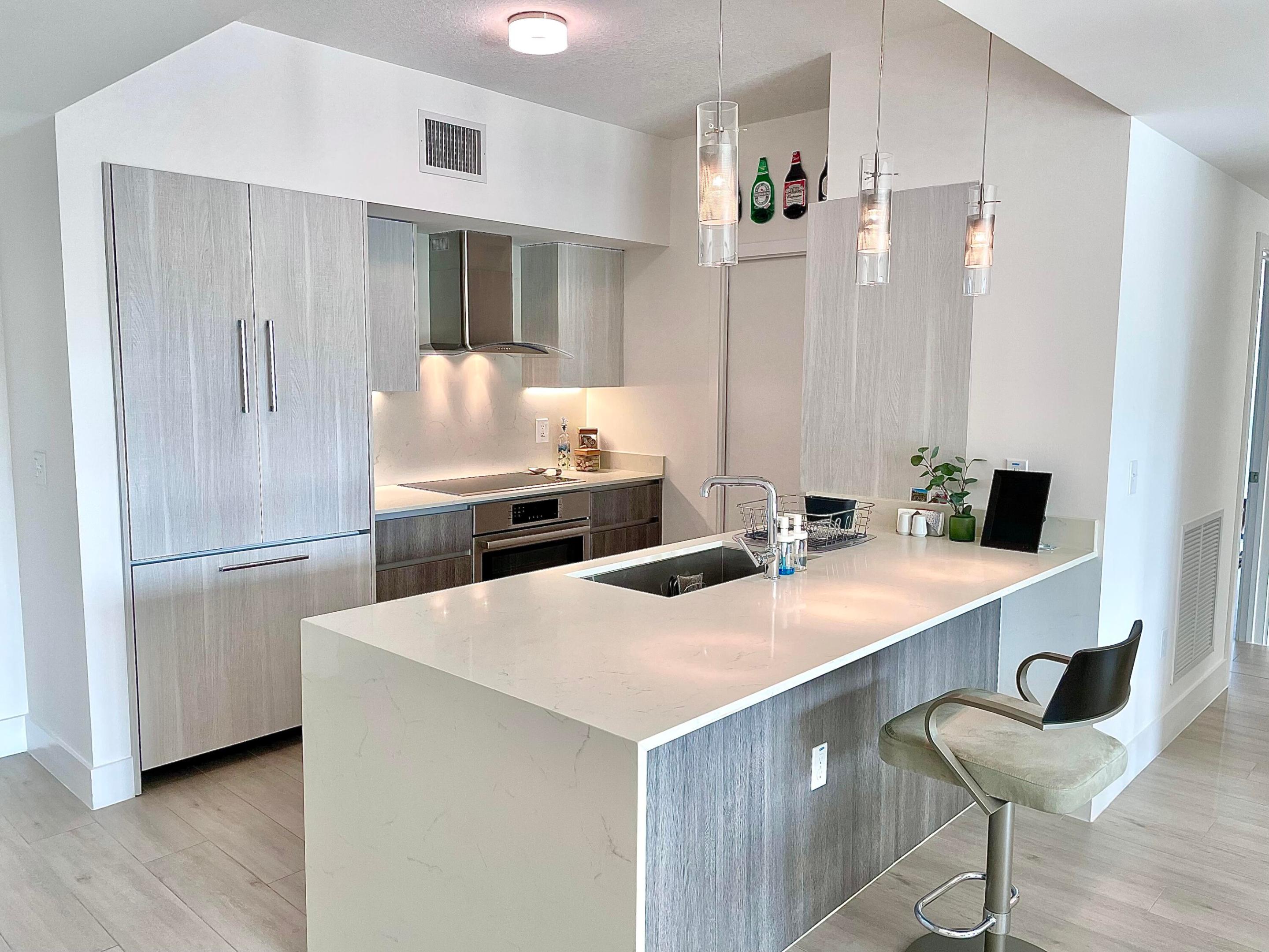Modern kitchen with gray cabinetry and a large white stone island beneath pendant lights.