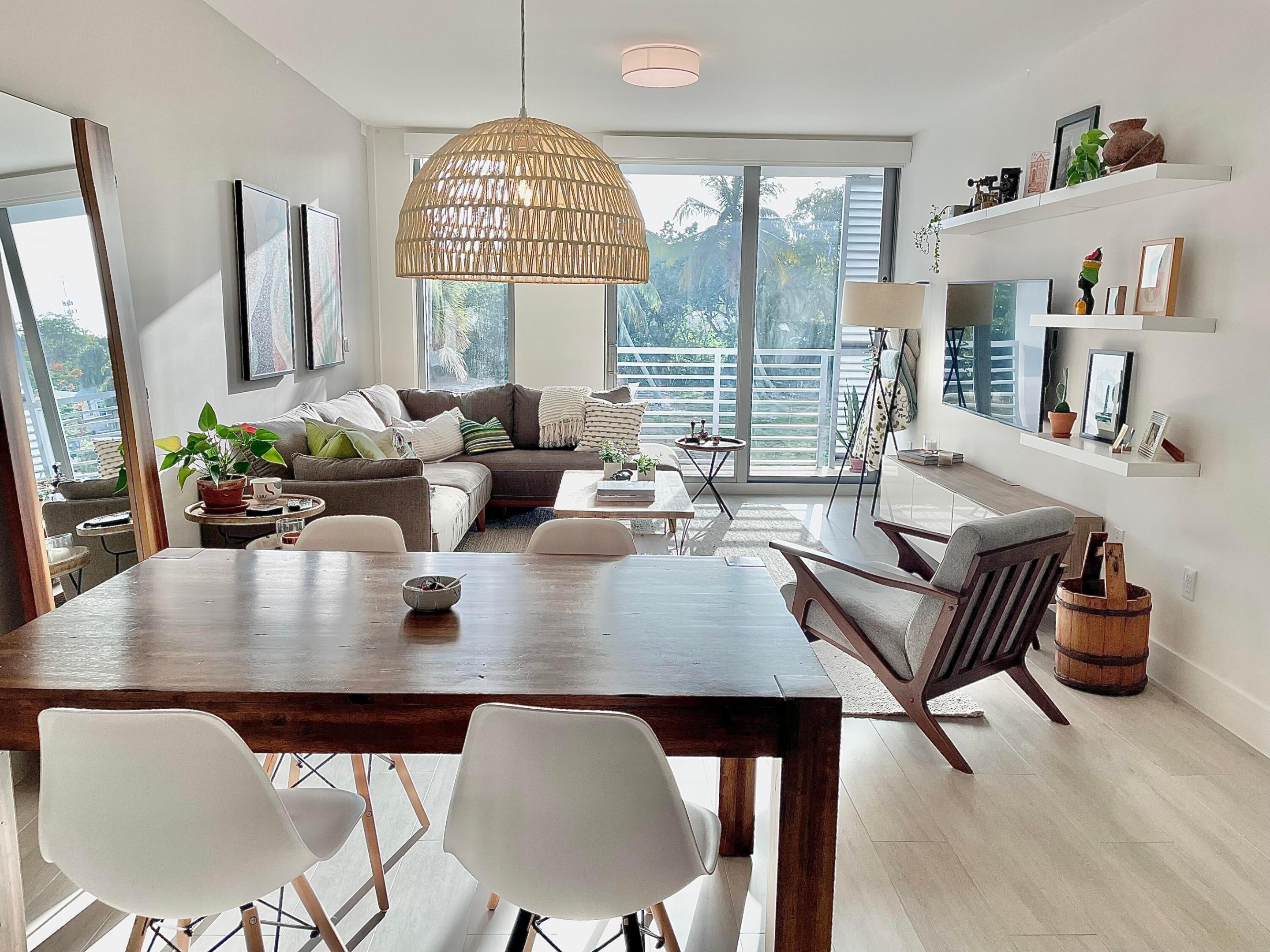 Open-plan condo living and dining room with a sectional sofa and balcony doors overlooking palm trees.