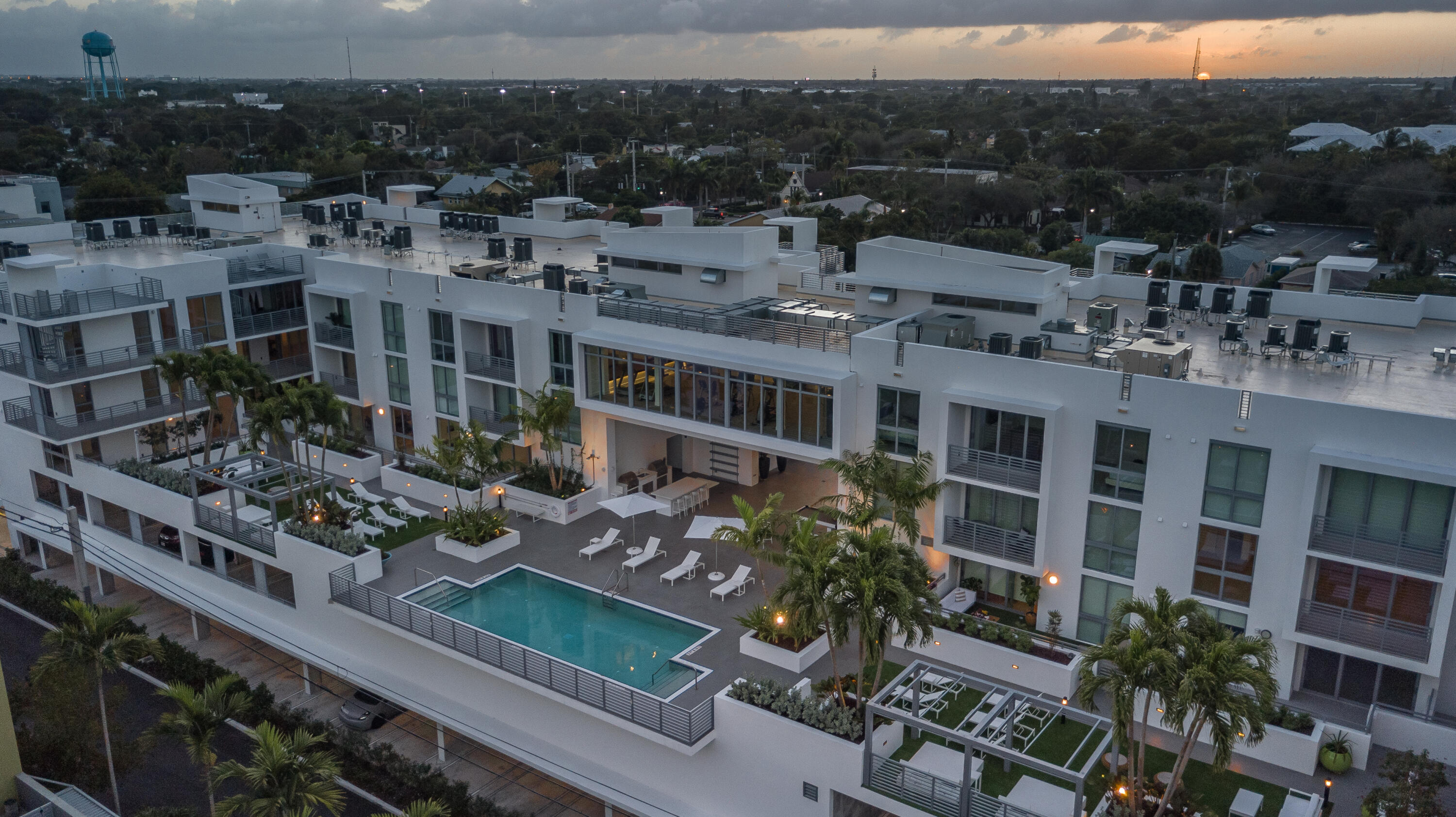 Modern condominium courtyard with a swimming pool, palm trees, and rooftop terraces at dusk.