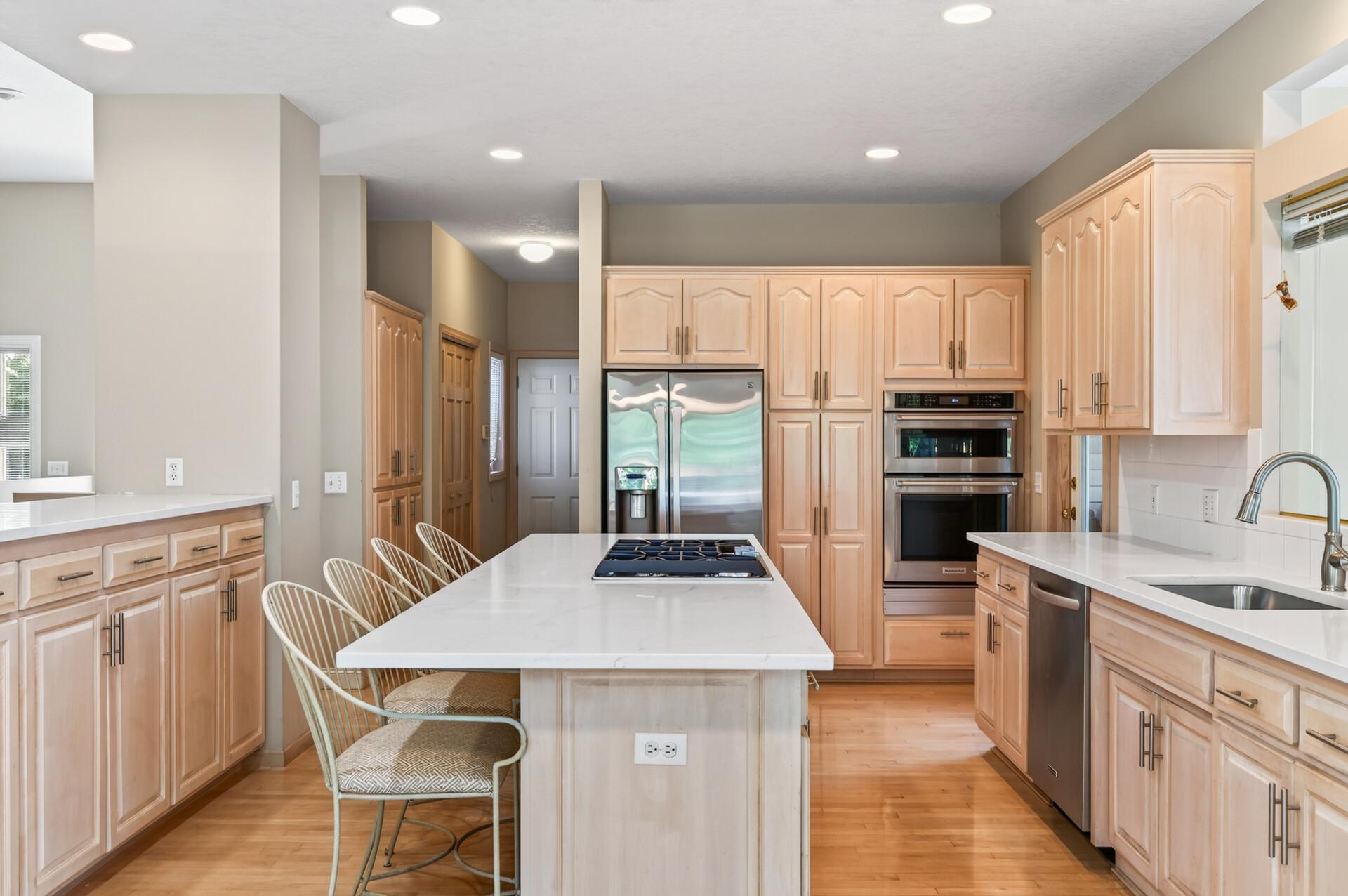 Kitchen with a large cooktop island, light wood cabinetry, stainless steel appliances, and hardwood floors.