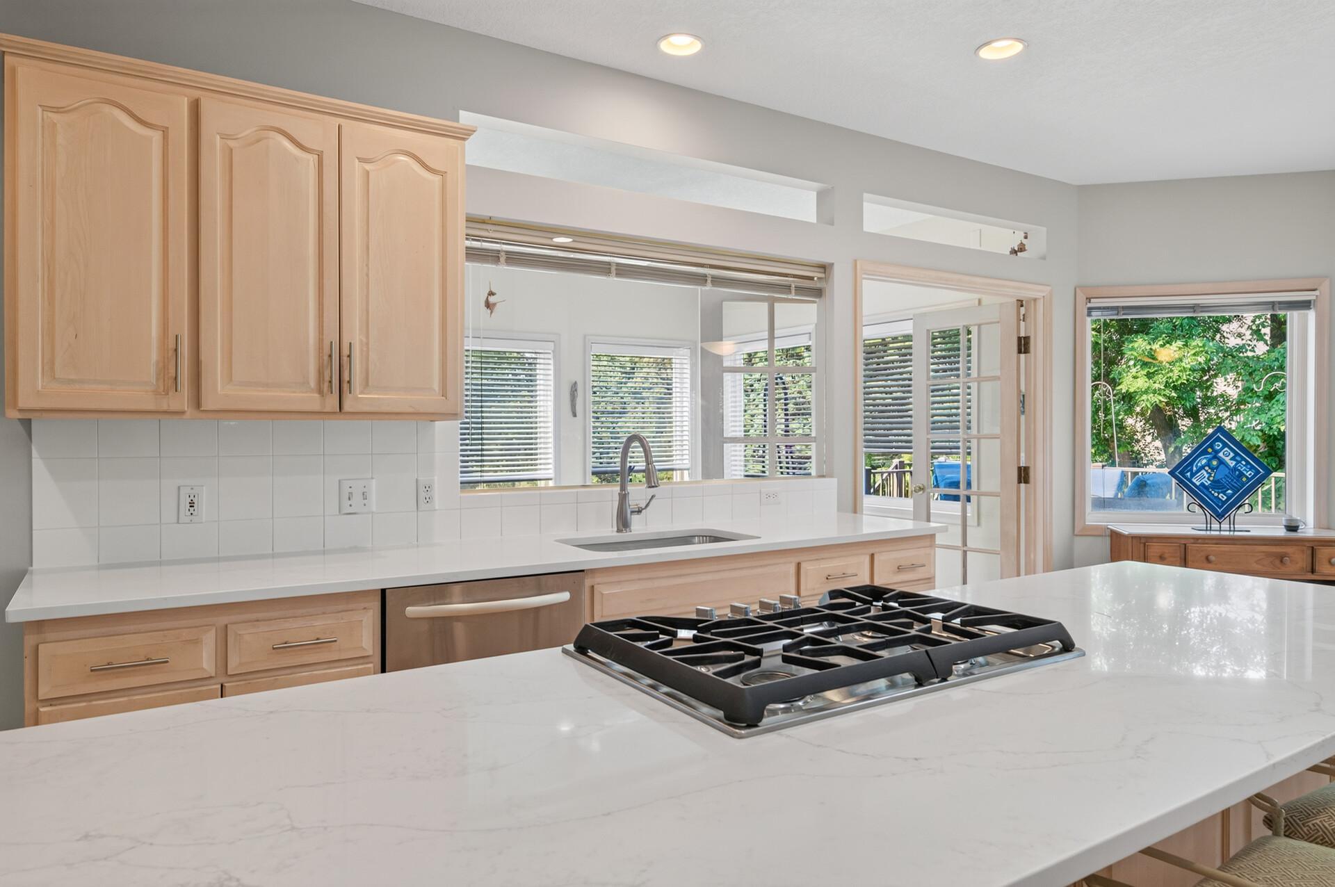 Kitchen with a large white island and gas cooktop, light wood cabinets, and a window-side sink.