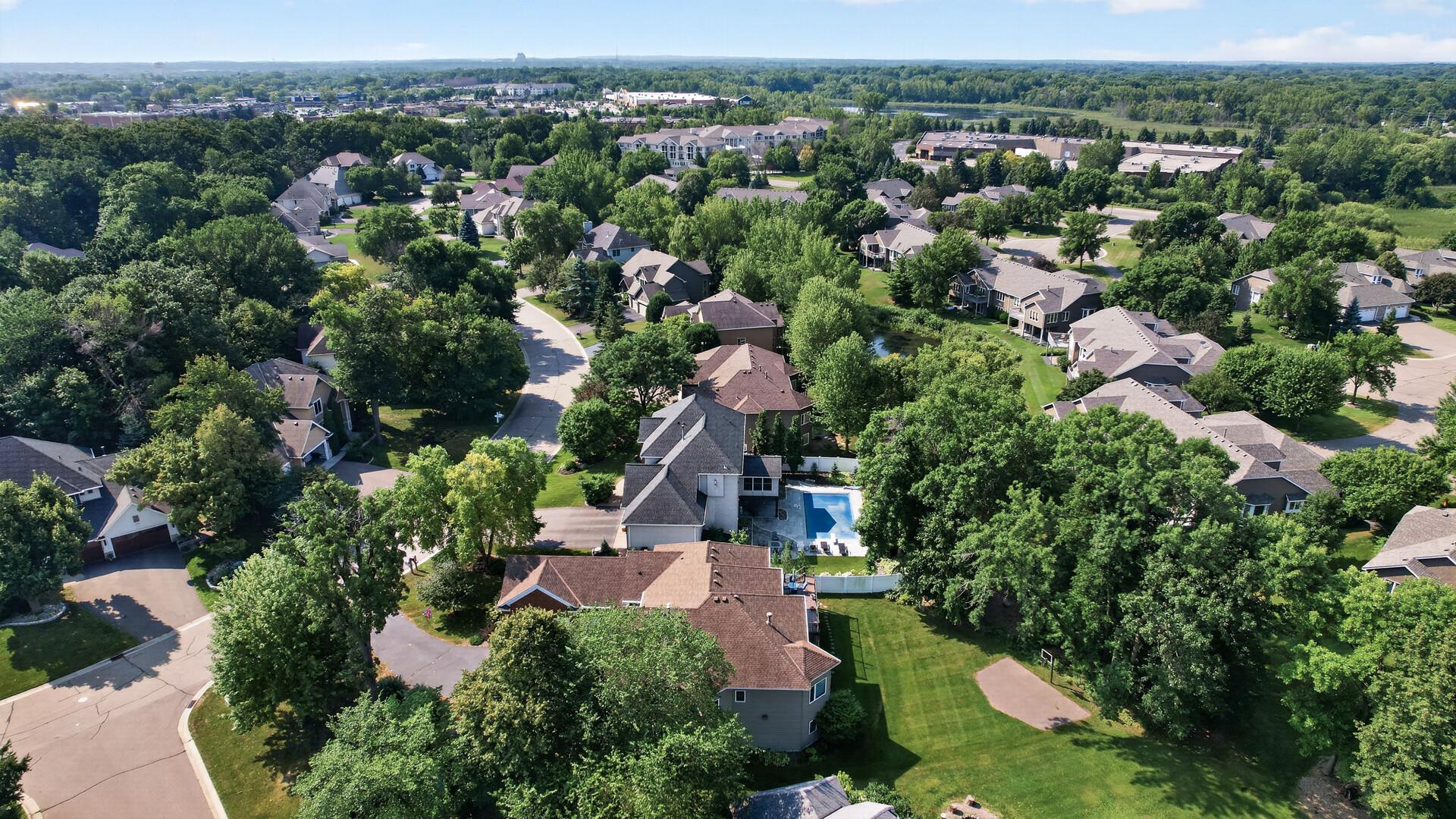 Aerial view of homes and a tree-lined neighborhood, with a backyard pool and curving streets.